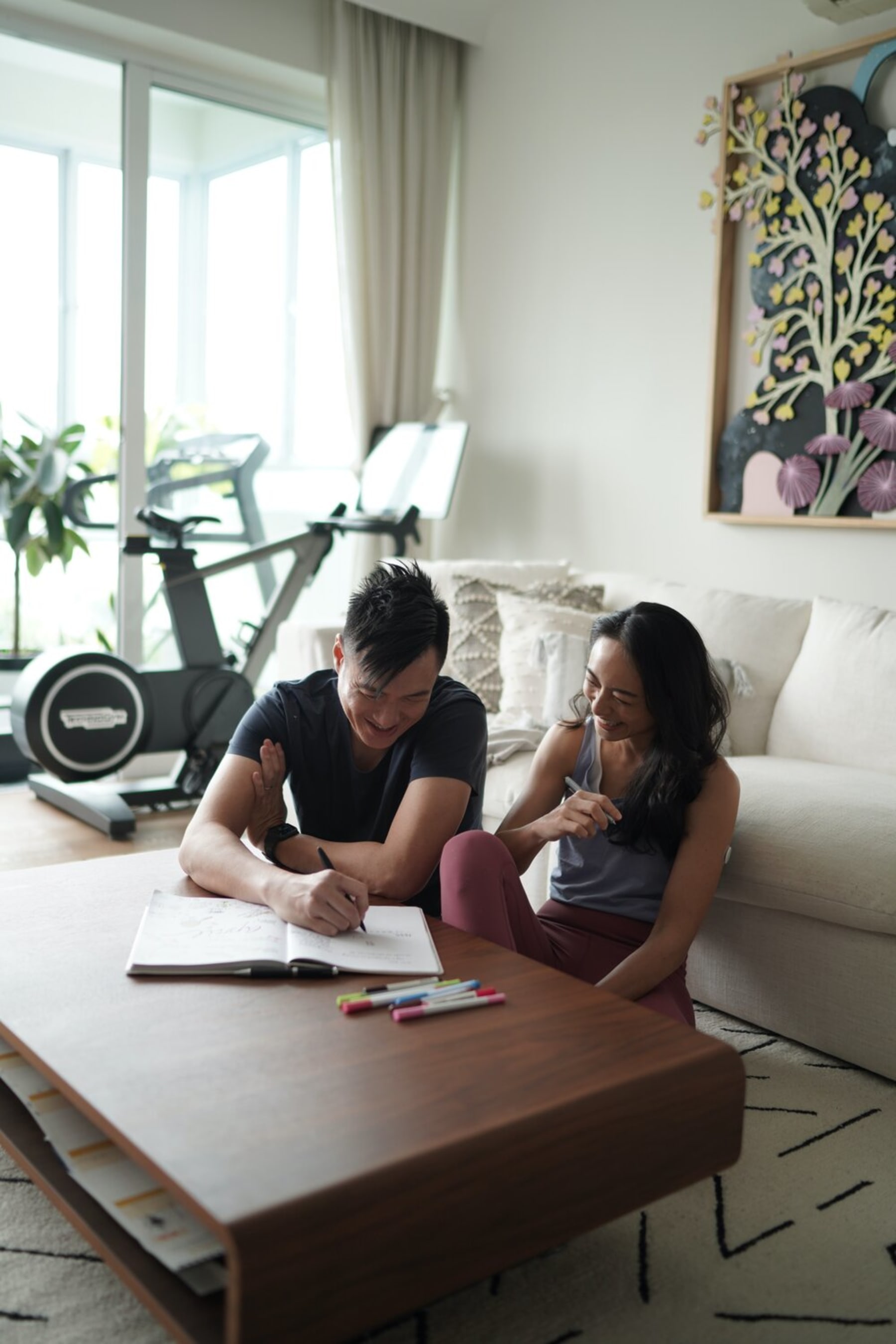 Two people are writing in a book on a wooden coffee table.