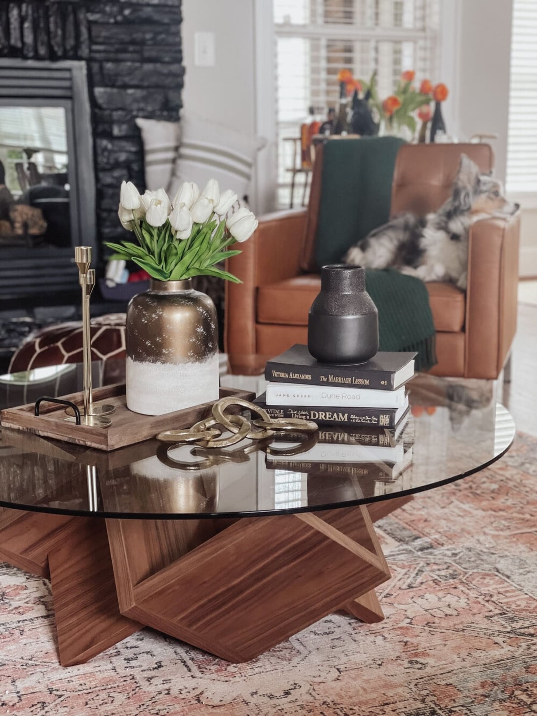 An artistic coffee table with a glass tabletop is decorated with books and vases.