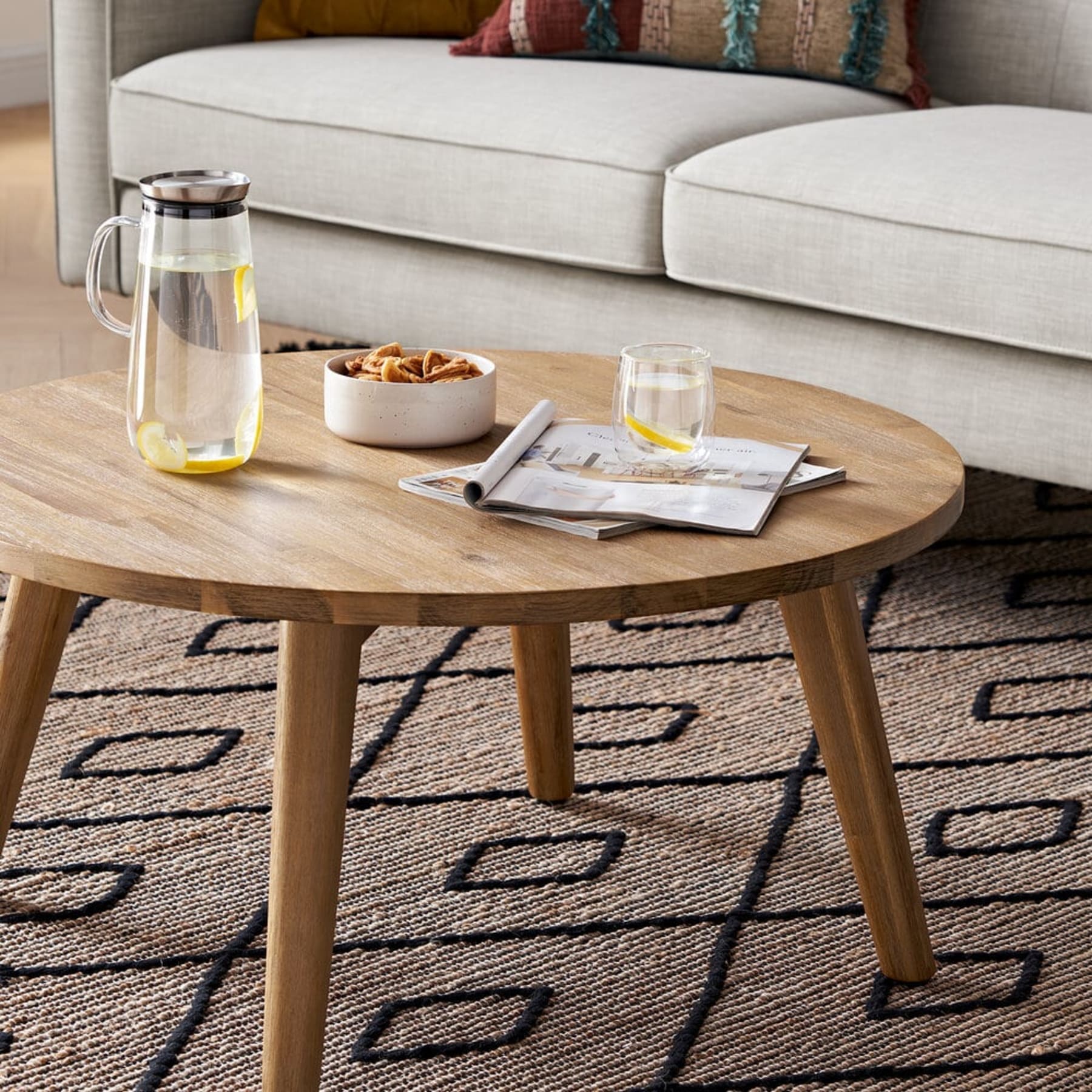 A wooden round coffee table with a magazine, glass, and bowl on top.