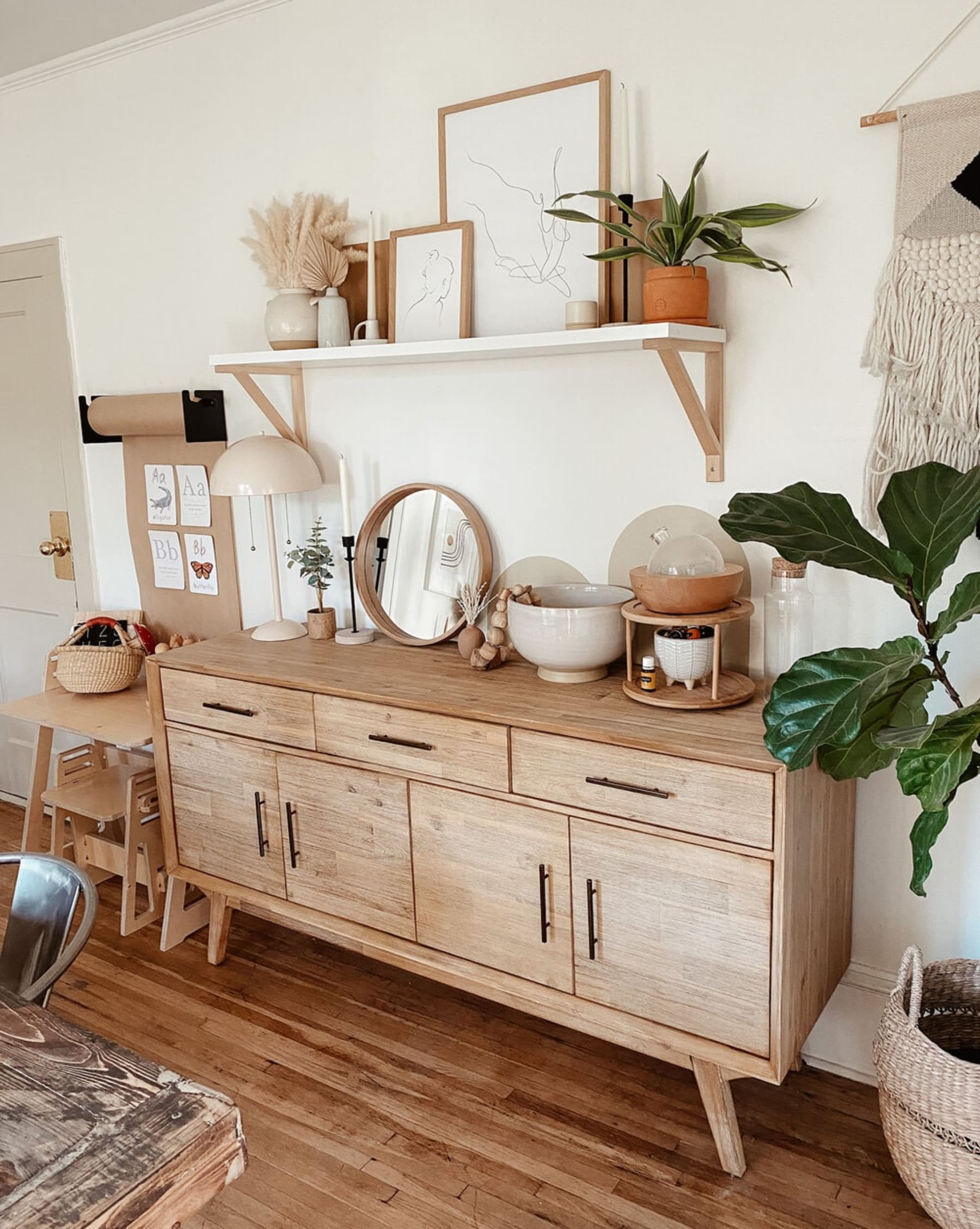 A sideboard with a picture frame and a speaker on top and wine glasses hanging above it.