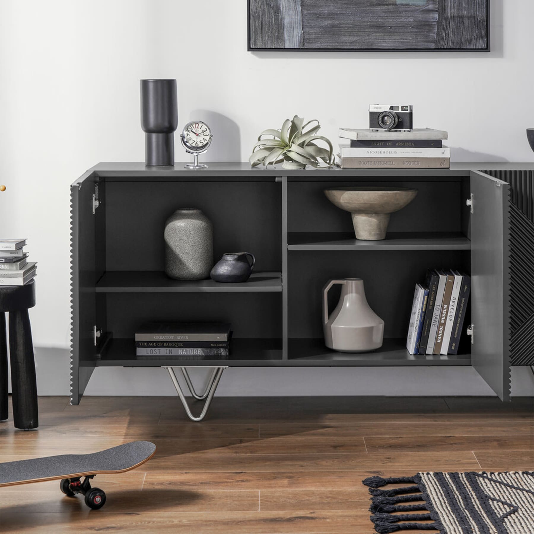 A black sideboard with its cabinet doors open shows books and decorative items inside.