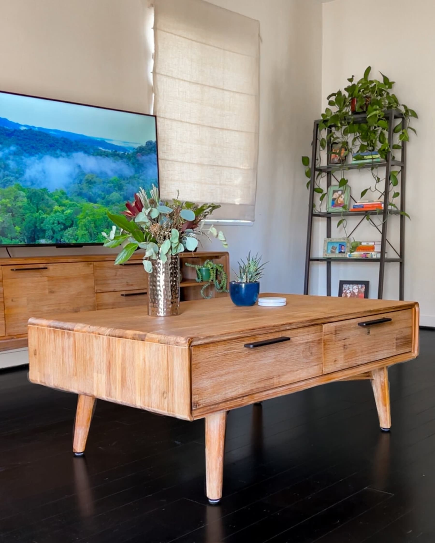 A wooden coffee table with 2 drawers and 2 potted plants on top.