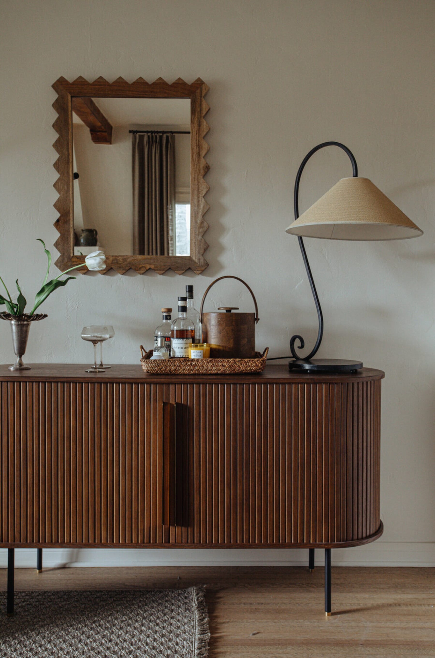 An oval sideboard with tambour doors with a woven tray and drinks.