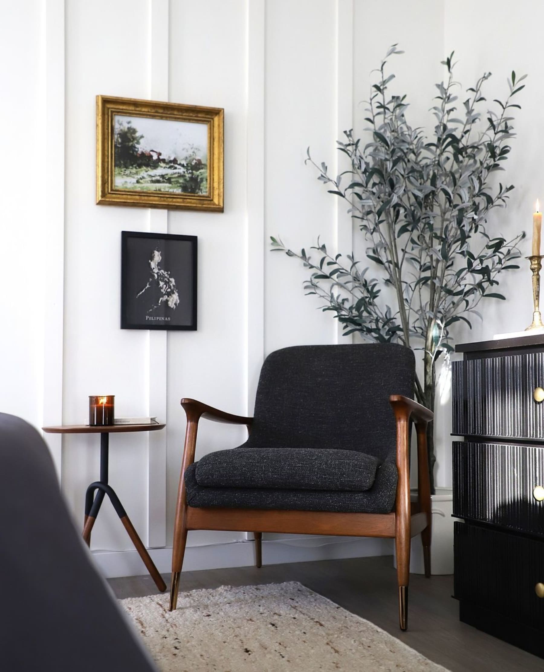 An armchair with dark fabric, wooden armrests, and brass-tipped legs.