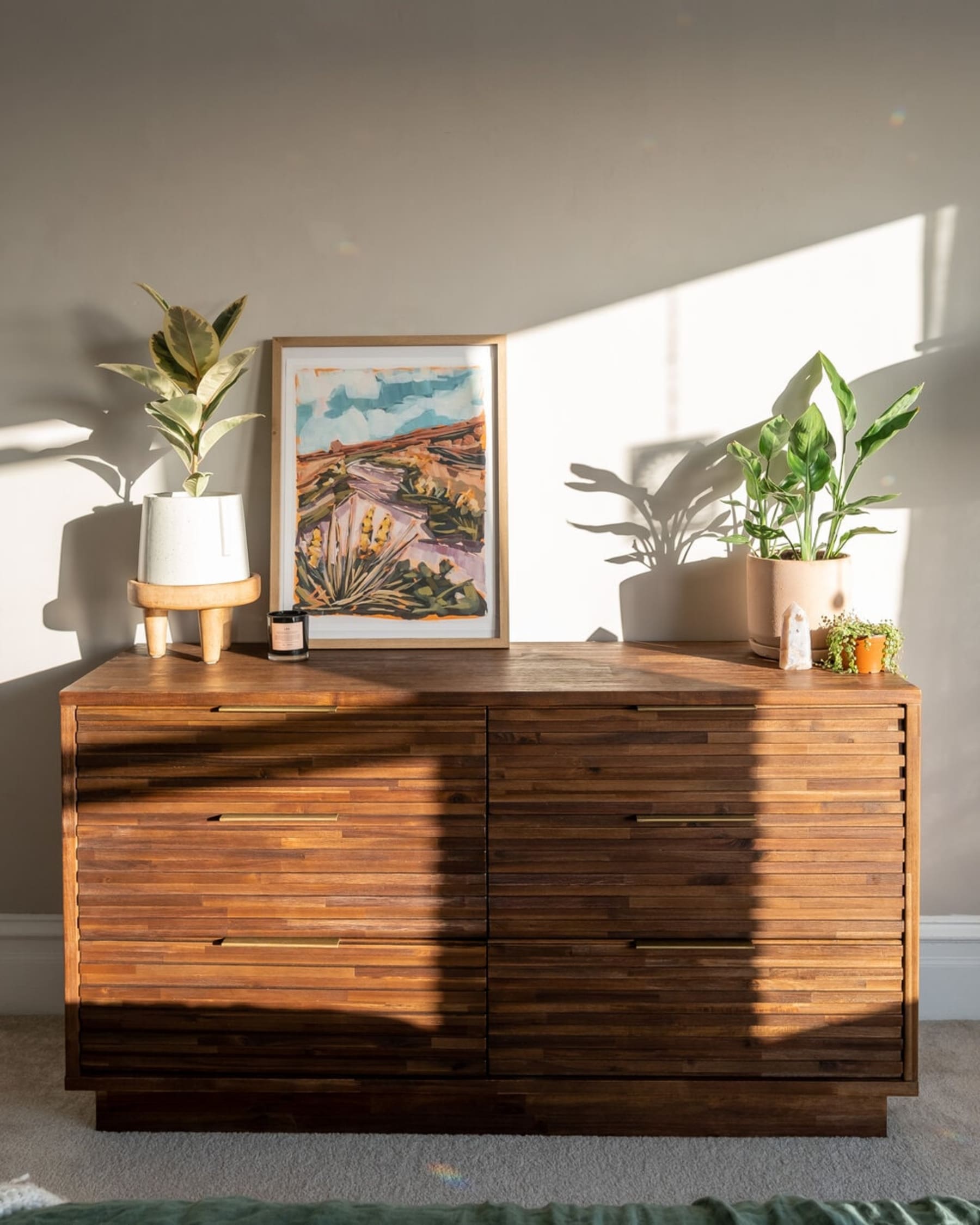 A dresser with fluted elements and brass handles and potted plants atop.