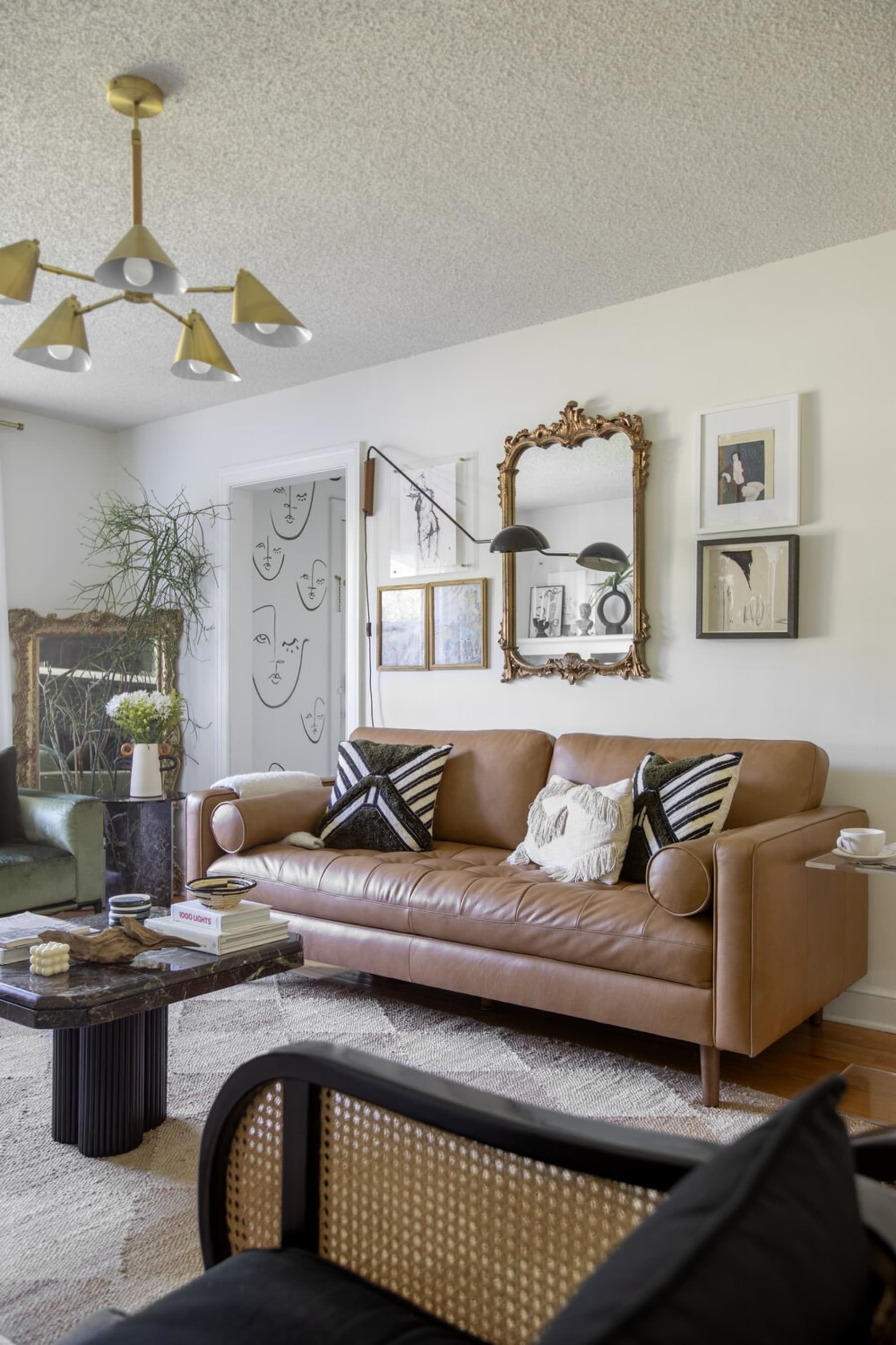 A vintage-looking mirror with a gold frame is hung above a leather sofa with tufted seats.