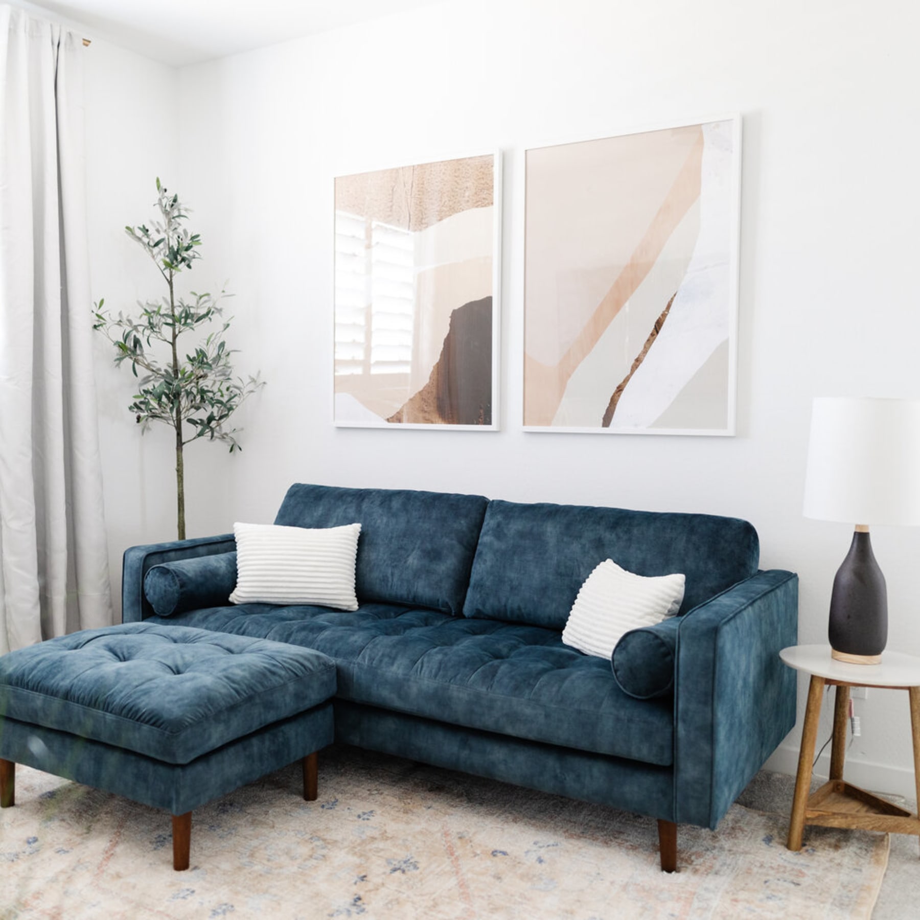 A dark blue velvet sofa and matching ottoman with contrasting white pillows.