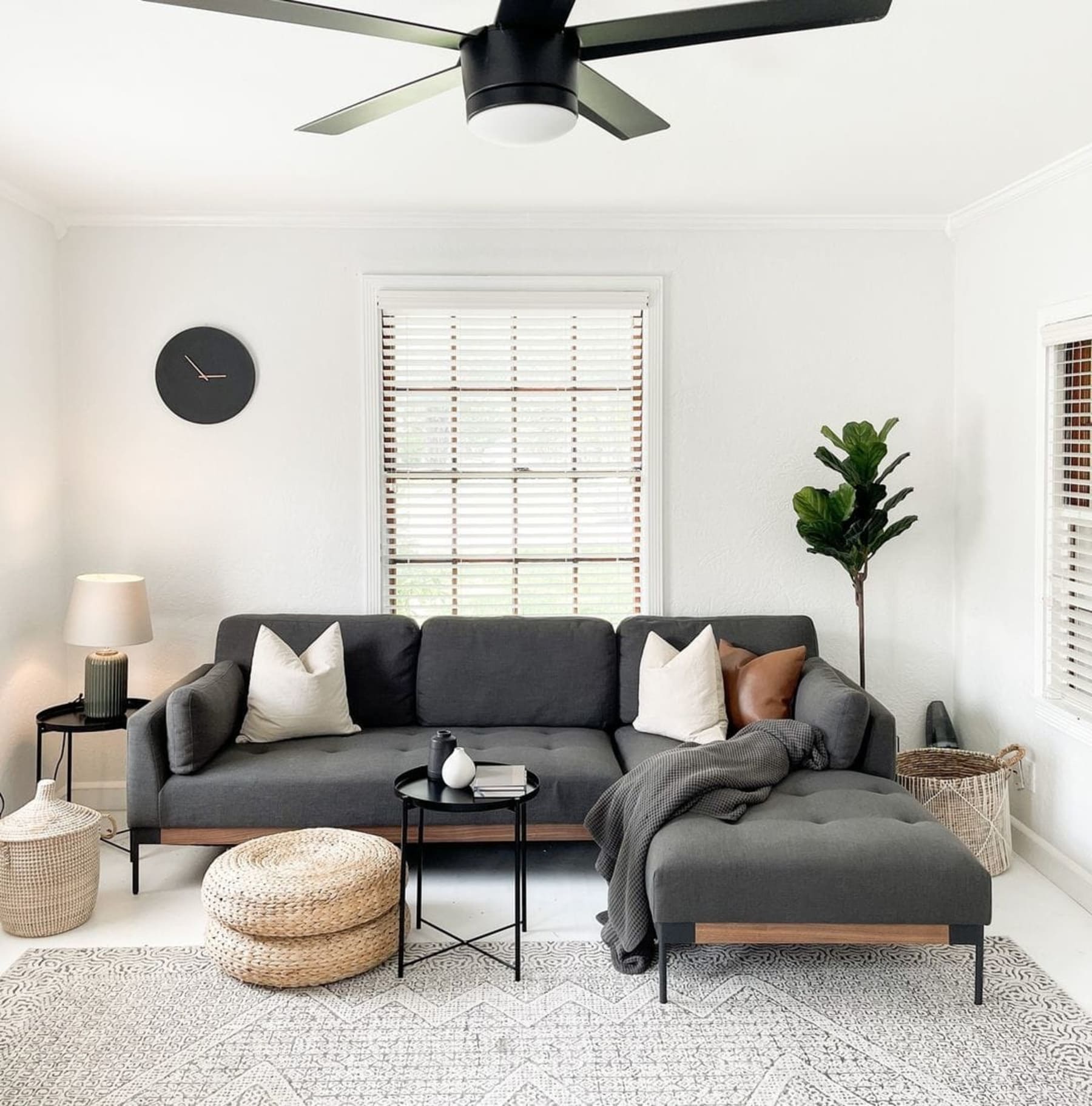 An L-shaped sectional sofa in a dark fabric and white pillows sits infront of a large window.