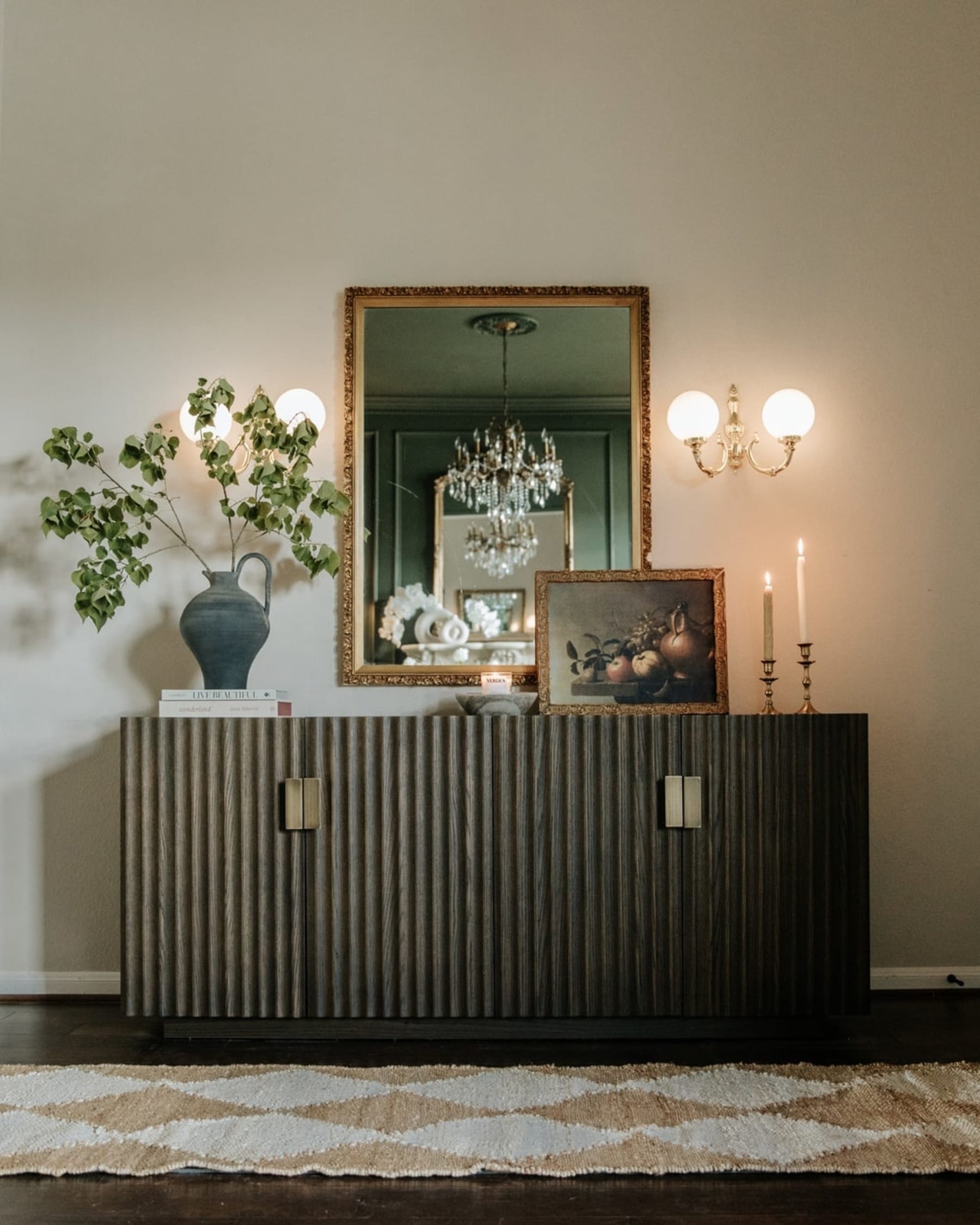 A black sideboard with fluted panels and brass handles decorated with candles, a photoframe, and a vase.