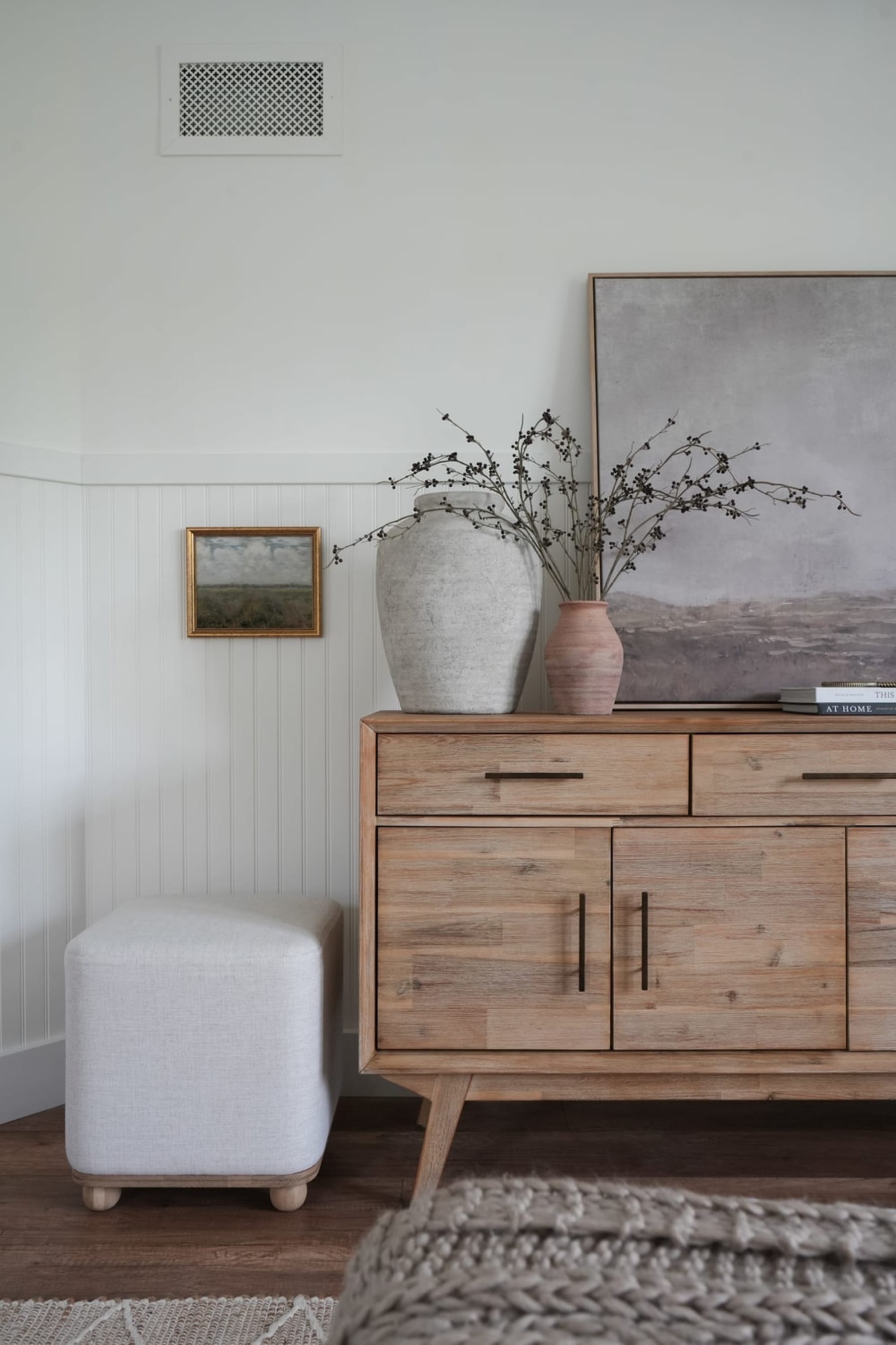 An ottoman placed next to a wooden sideboard.