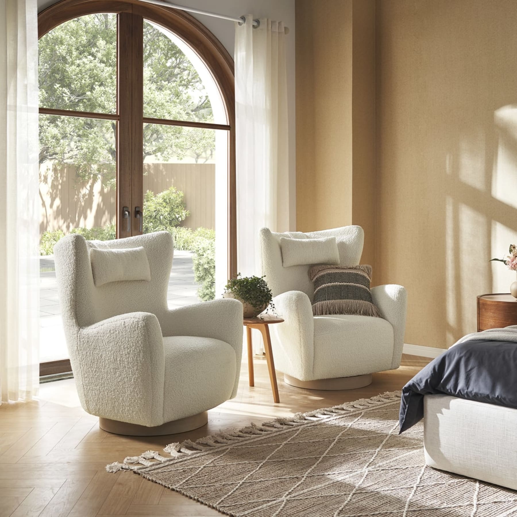 Two swivel armchairs with a side table placed between them in a bedroom.