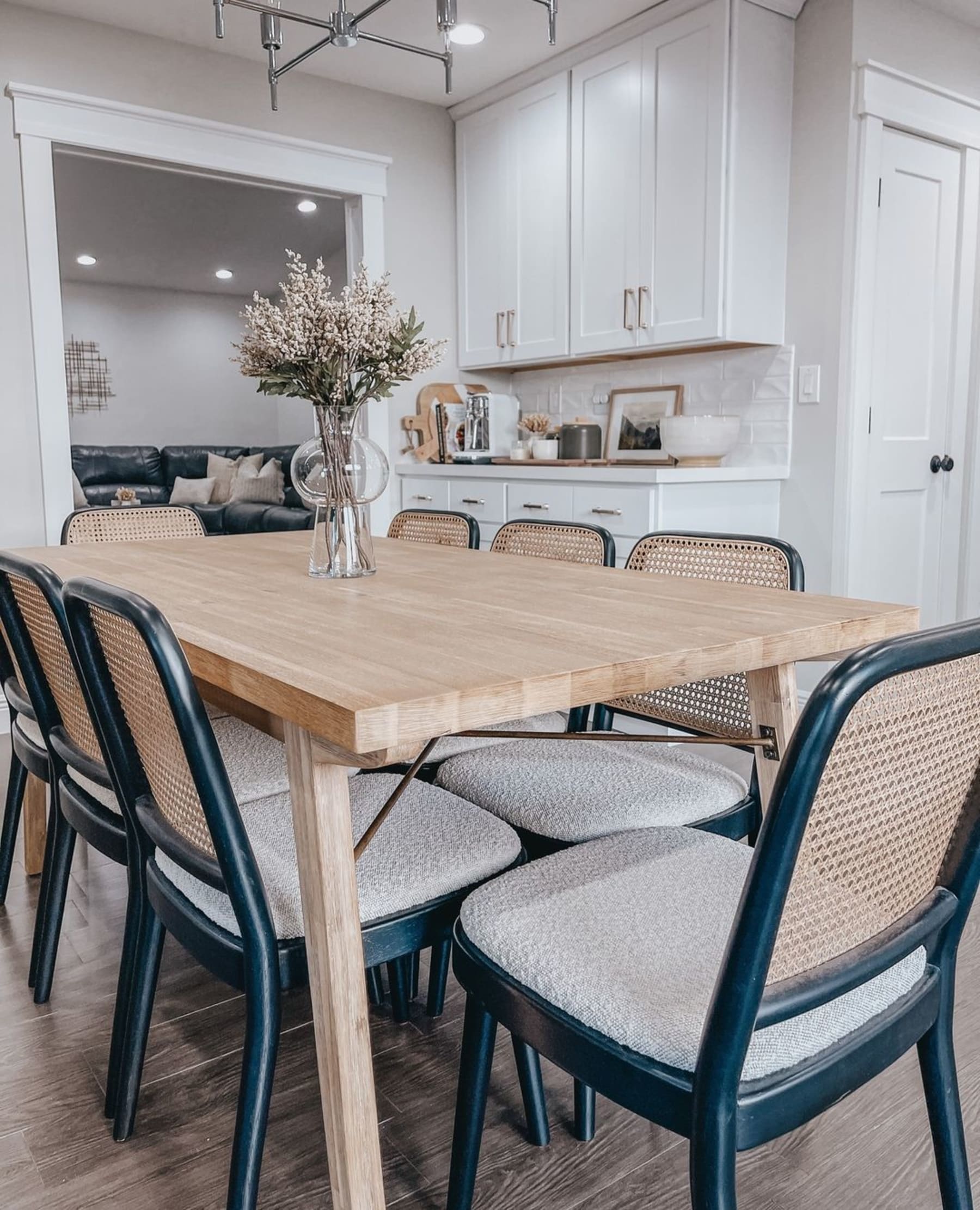 A white-washed wooden dining table paired with black cane chairs.