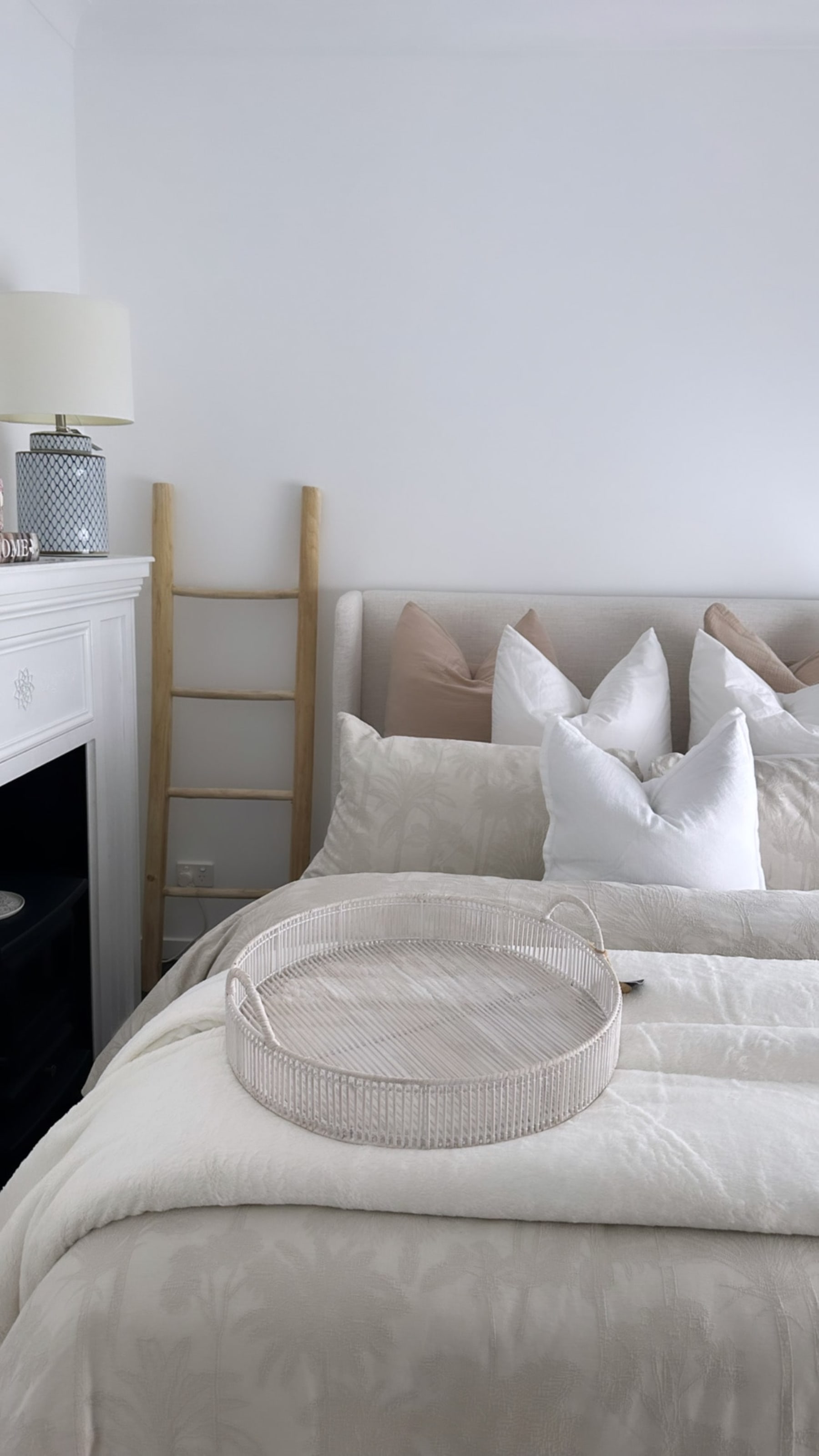 A bed with a wingback headboard and neutral-colored cushions.