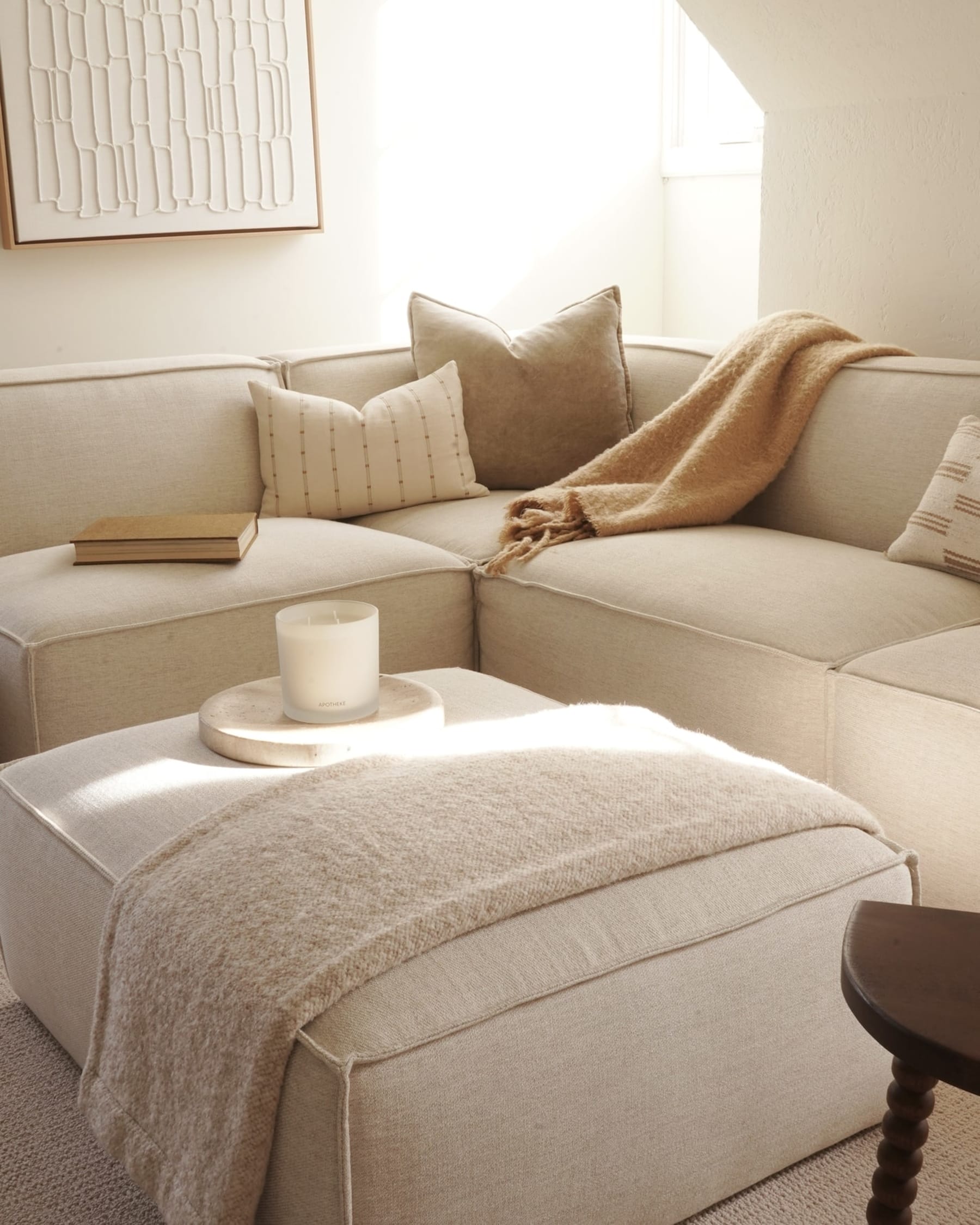 A fabric ottoman with a candle placed on top is being used as a coffee table.