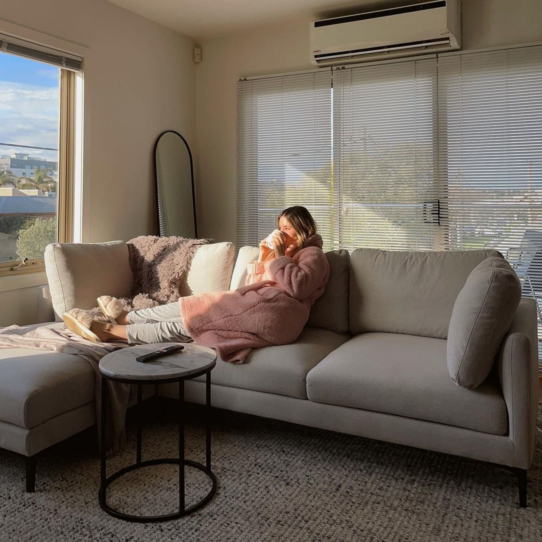 A person is sitting on a chaise sectional sofa with the sunlight shining into the room.