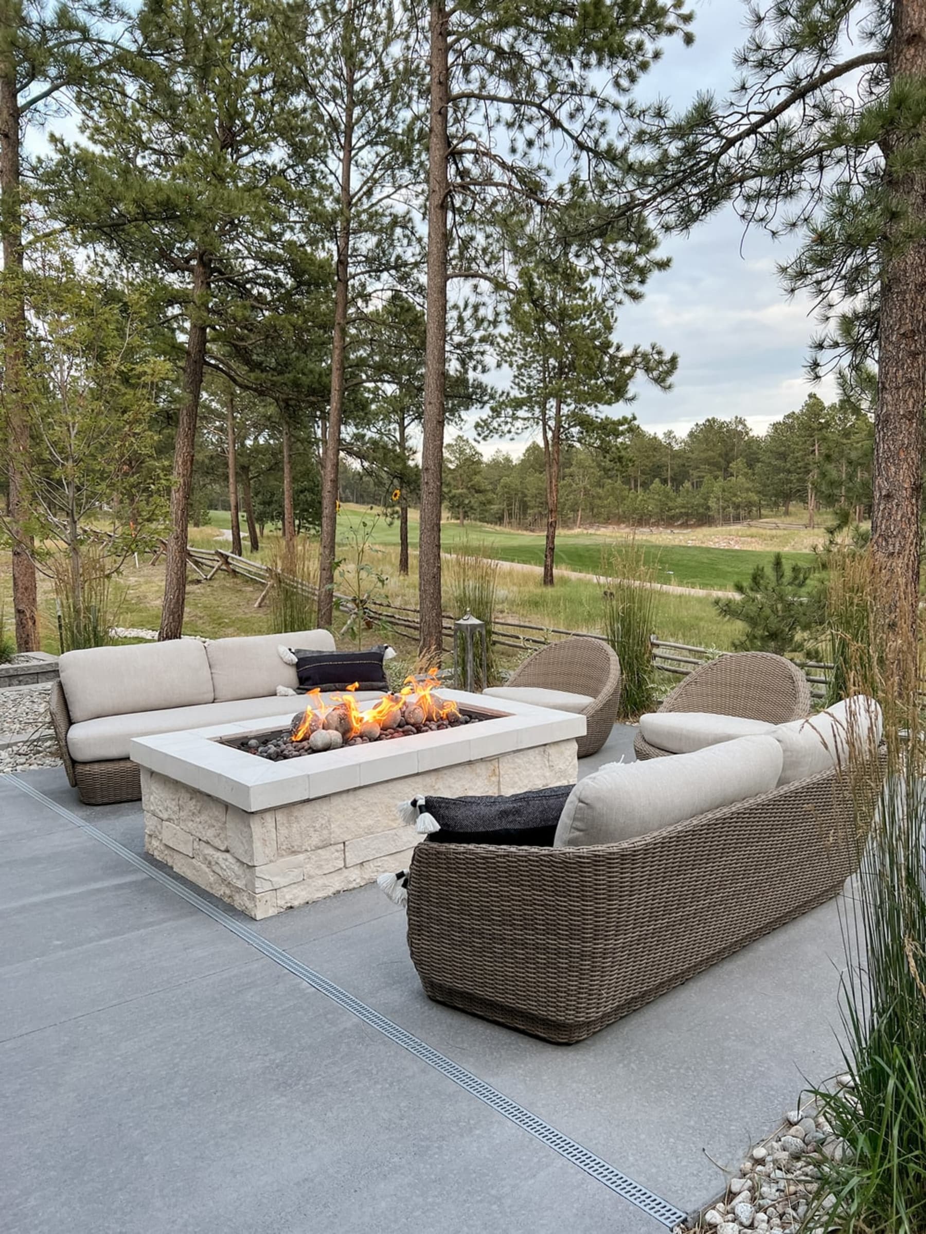 Two wicker sofas and matching lounge chairs surround an outdoor fireplace.