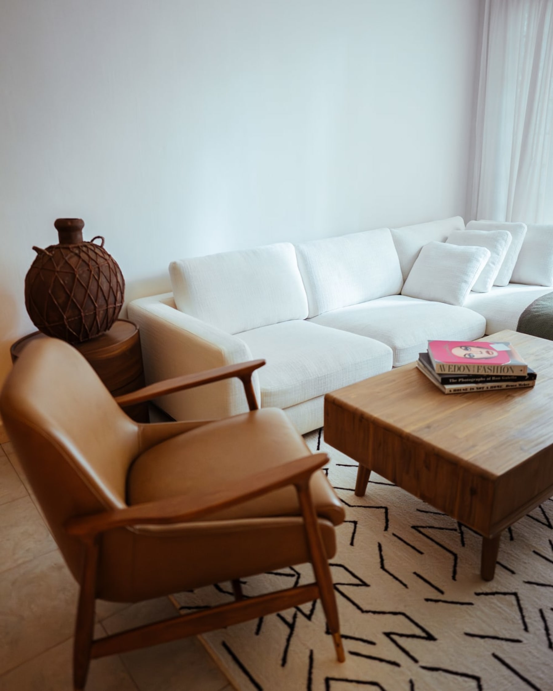 A leather armchair, wooden coffee table, and white fabric sectional chaise sofa.