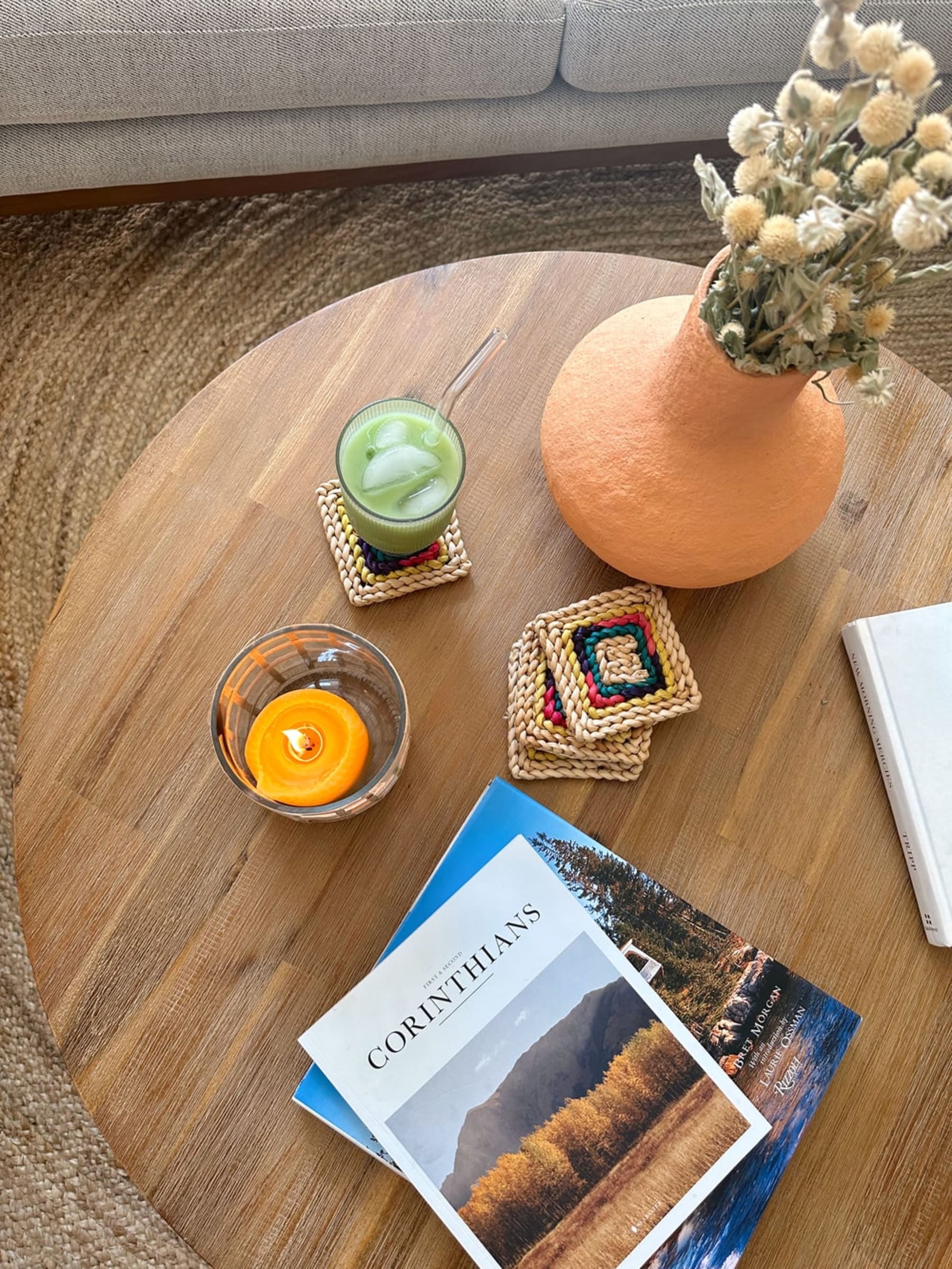 A round acacia wood coffee table with books, a candle, a vase, and a cup atop.