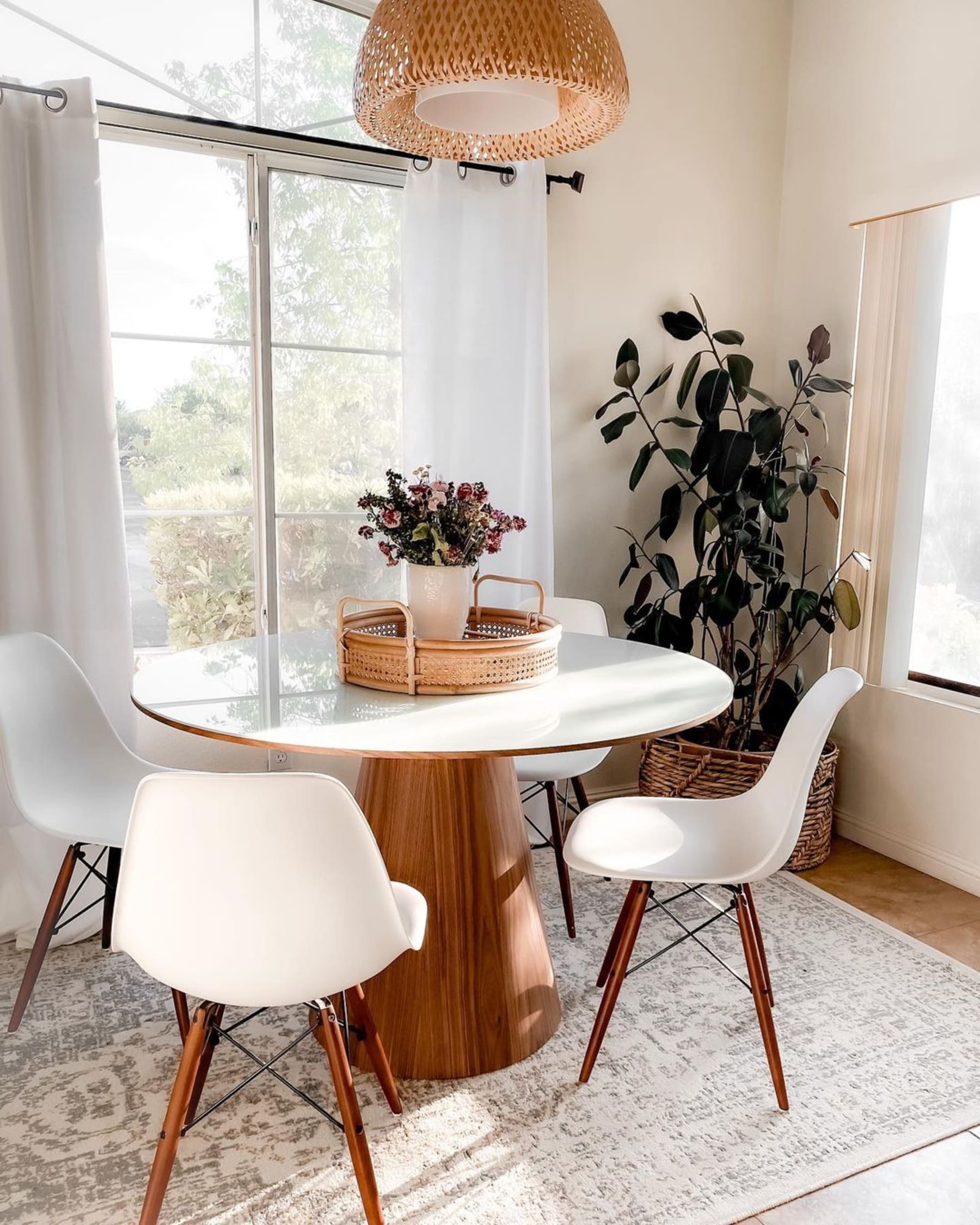 A round dining table with a glass surface and a woven basket and vase of flowers as the centrepiece.