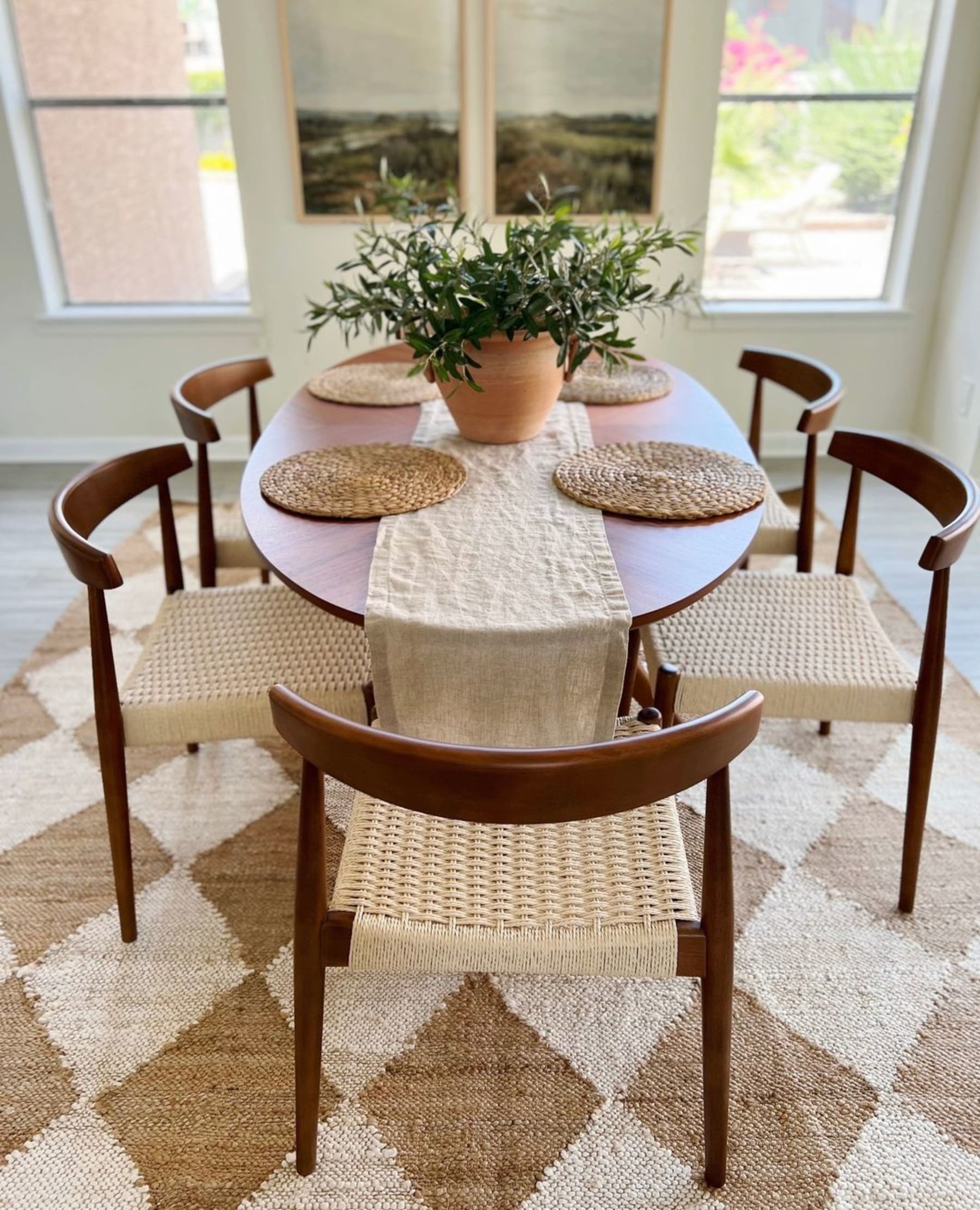 An oval wooden dining table with placemats, a runner, and a potted plant.