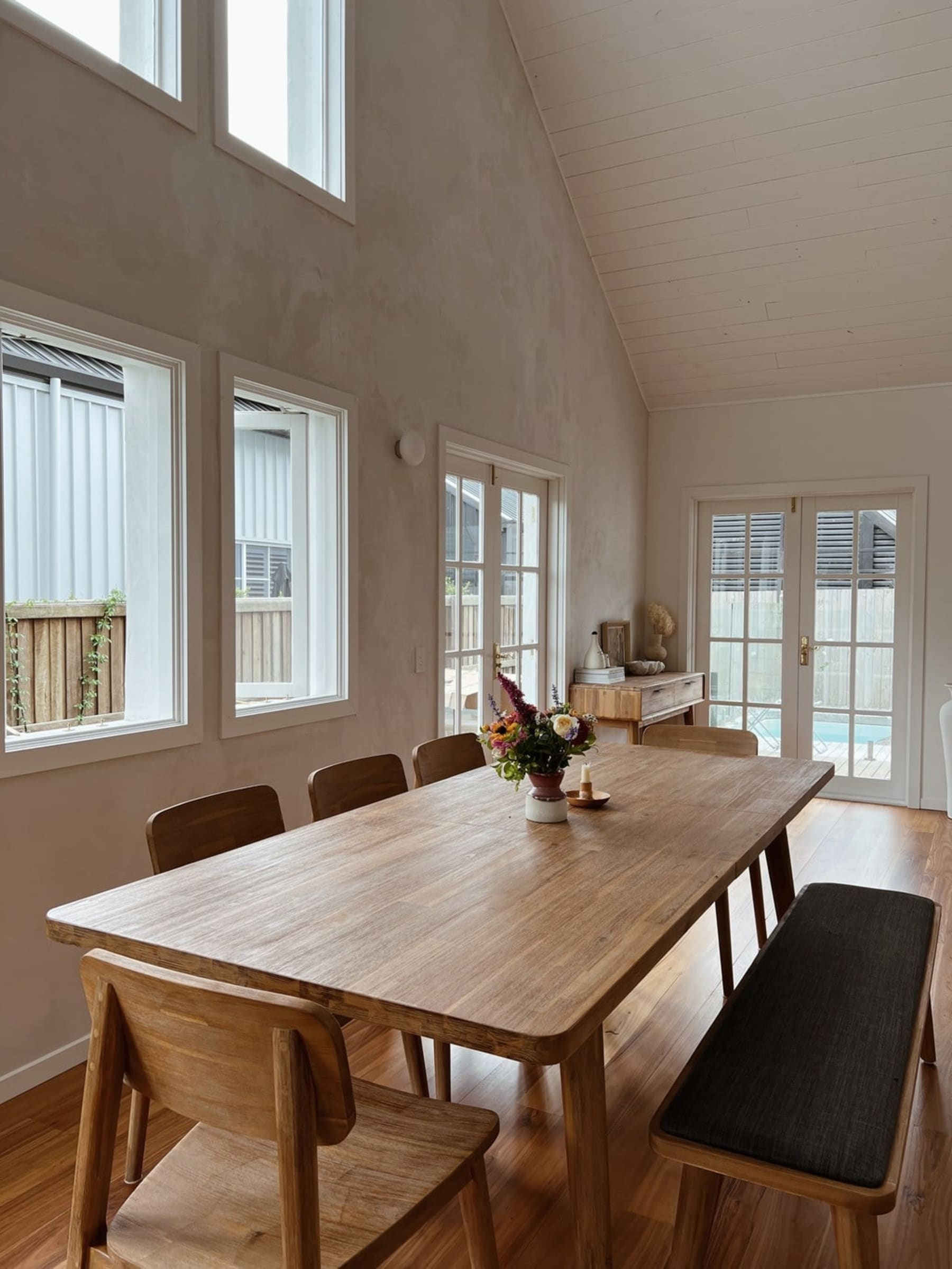 An extendable wooden dining table set with a small vase of flowers in the center.