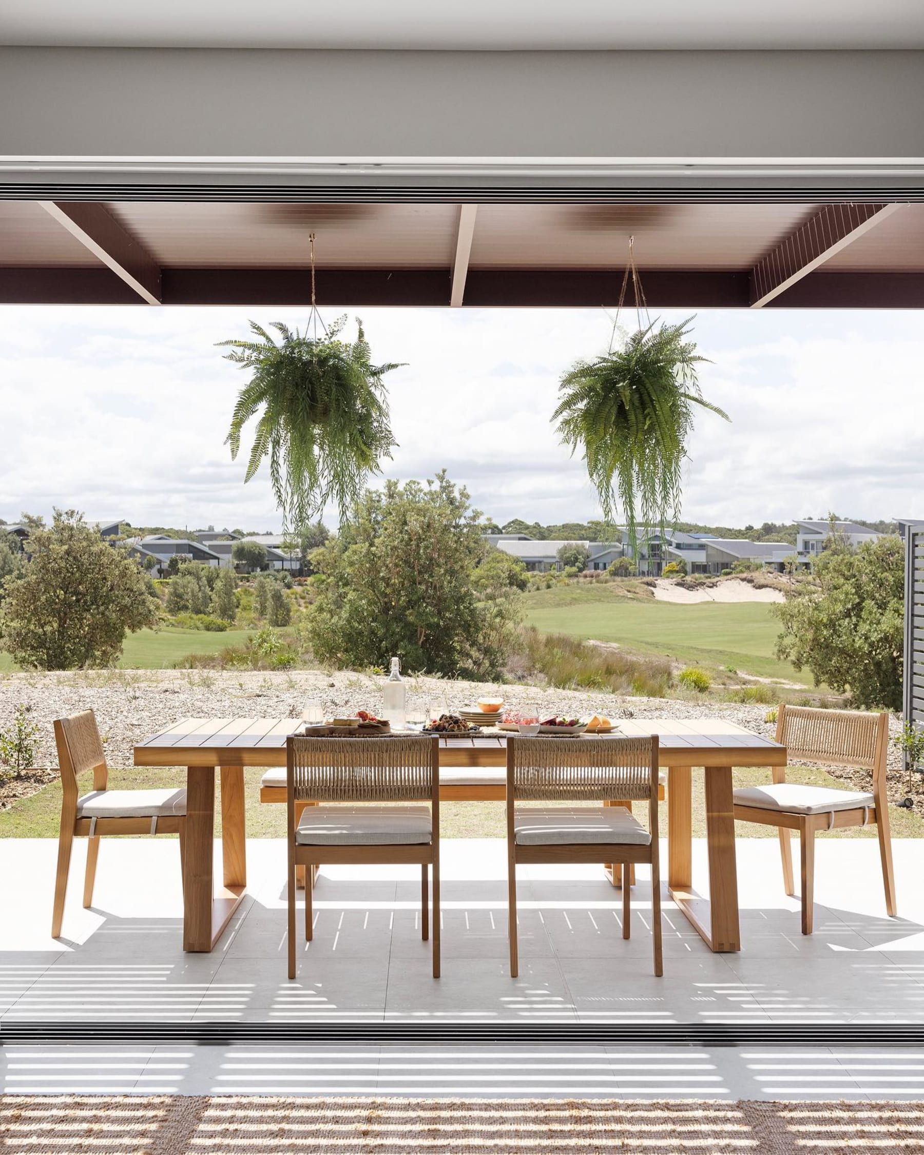 A teak outdoor dining set placed in the backyard by a pool.