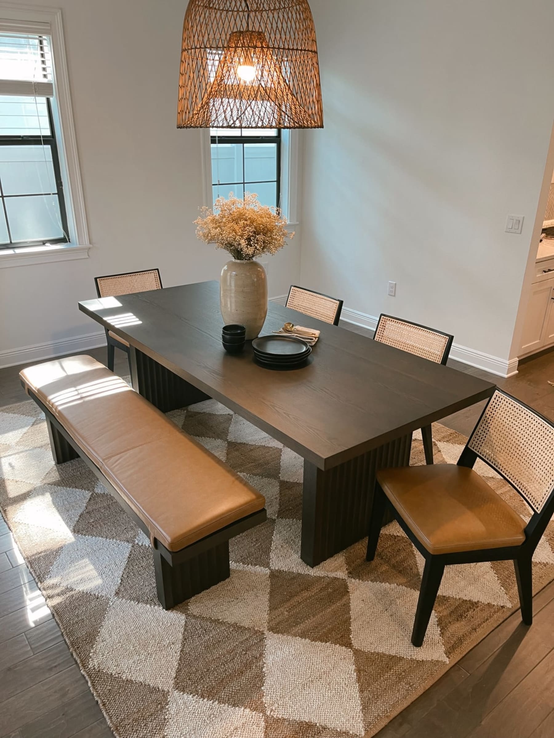 A black wooden dining table with matching leather chairs and a bench.