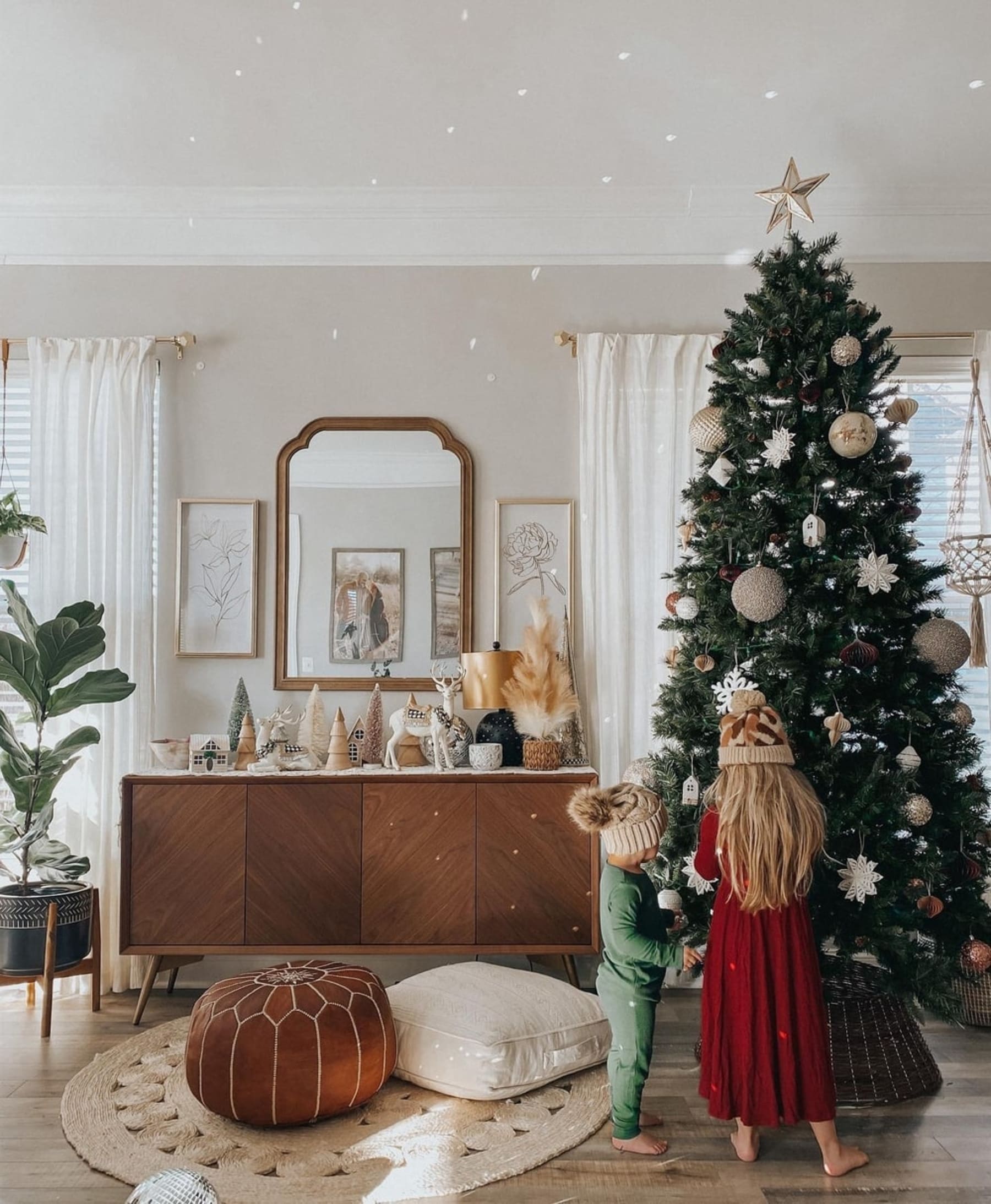 Two children decorating a Christmas tree with ornaments beside a wooden sideboard.