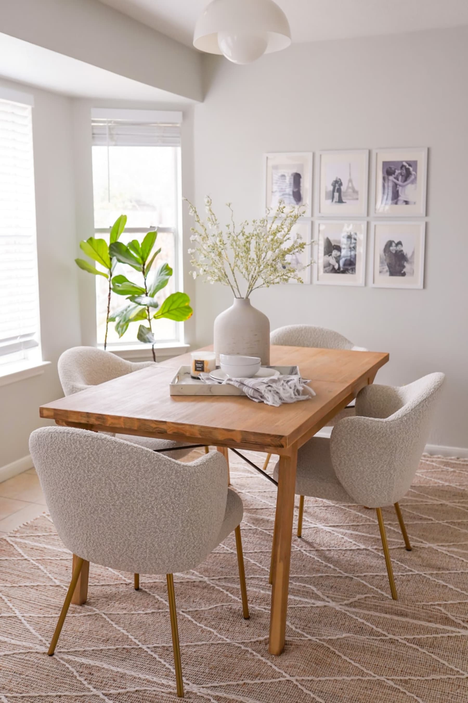 A wooden dining table with four chairs and a gallery wall behind it.