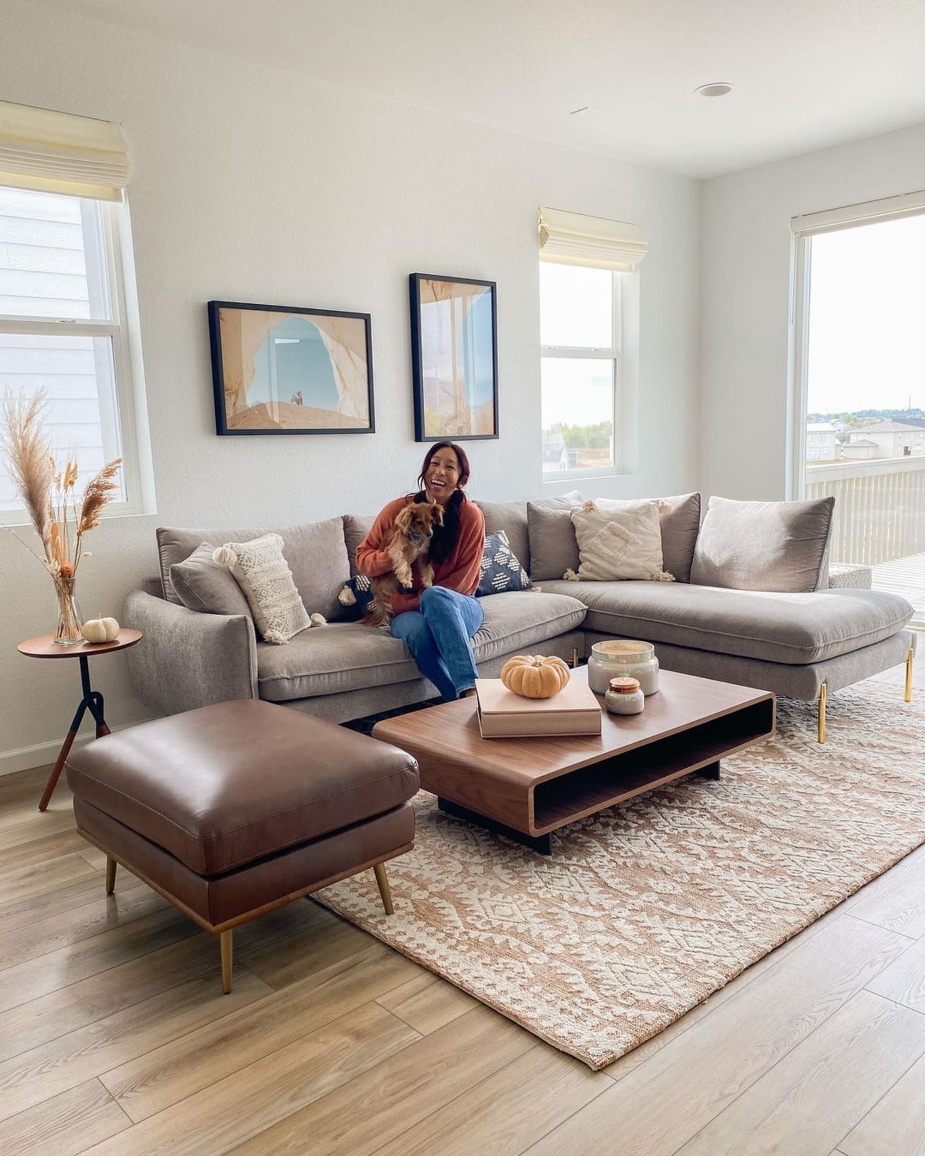 A person holding their pet dog sitting on a gray bumper chaise sectional sofa.