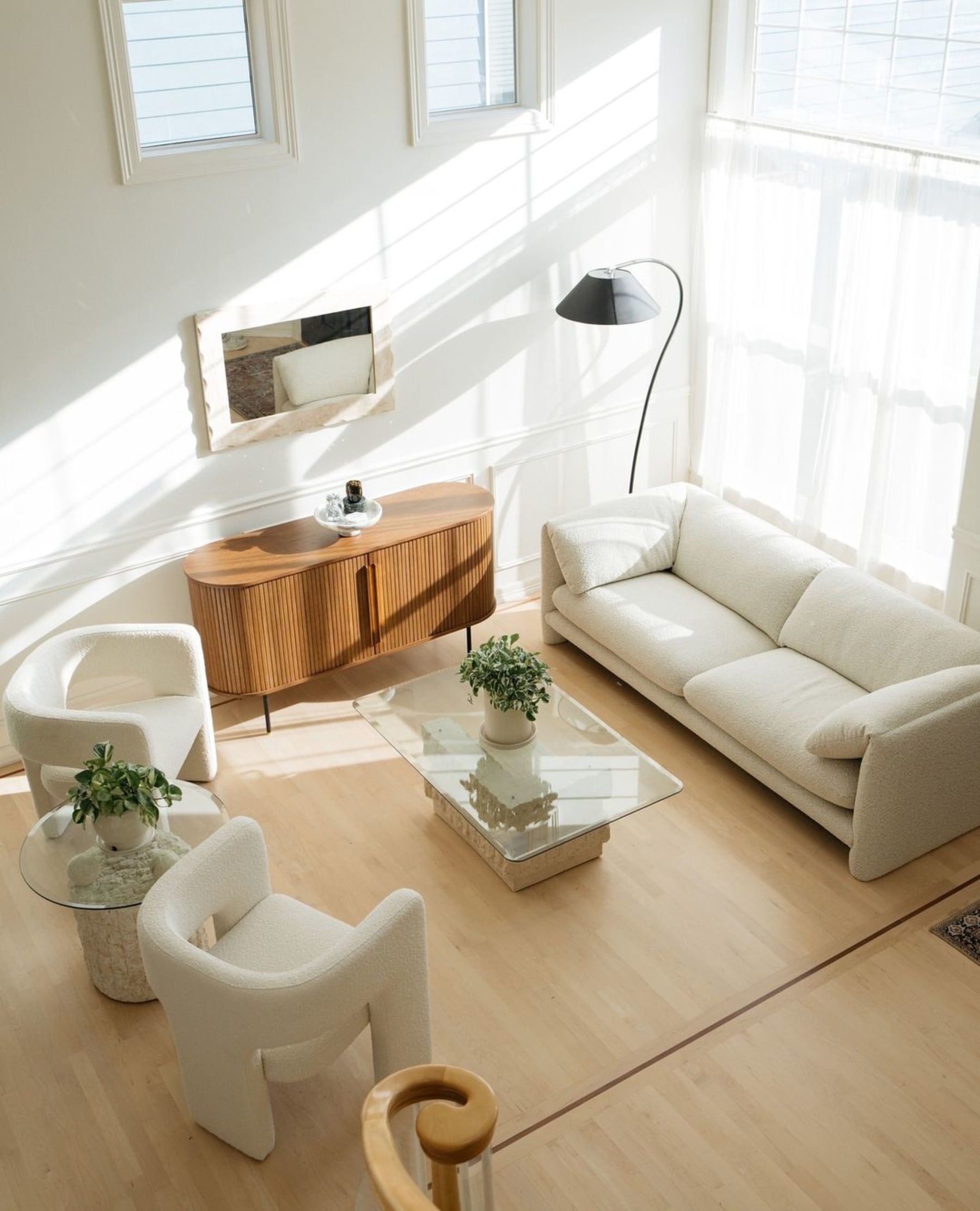 A bouclé sofa in a living room with two armchairs, a glass coffee table, and tambour door sideboard.