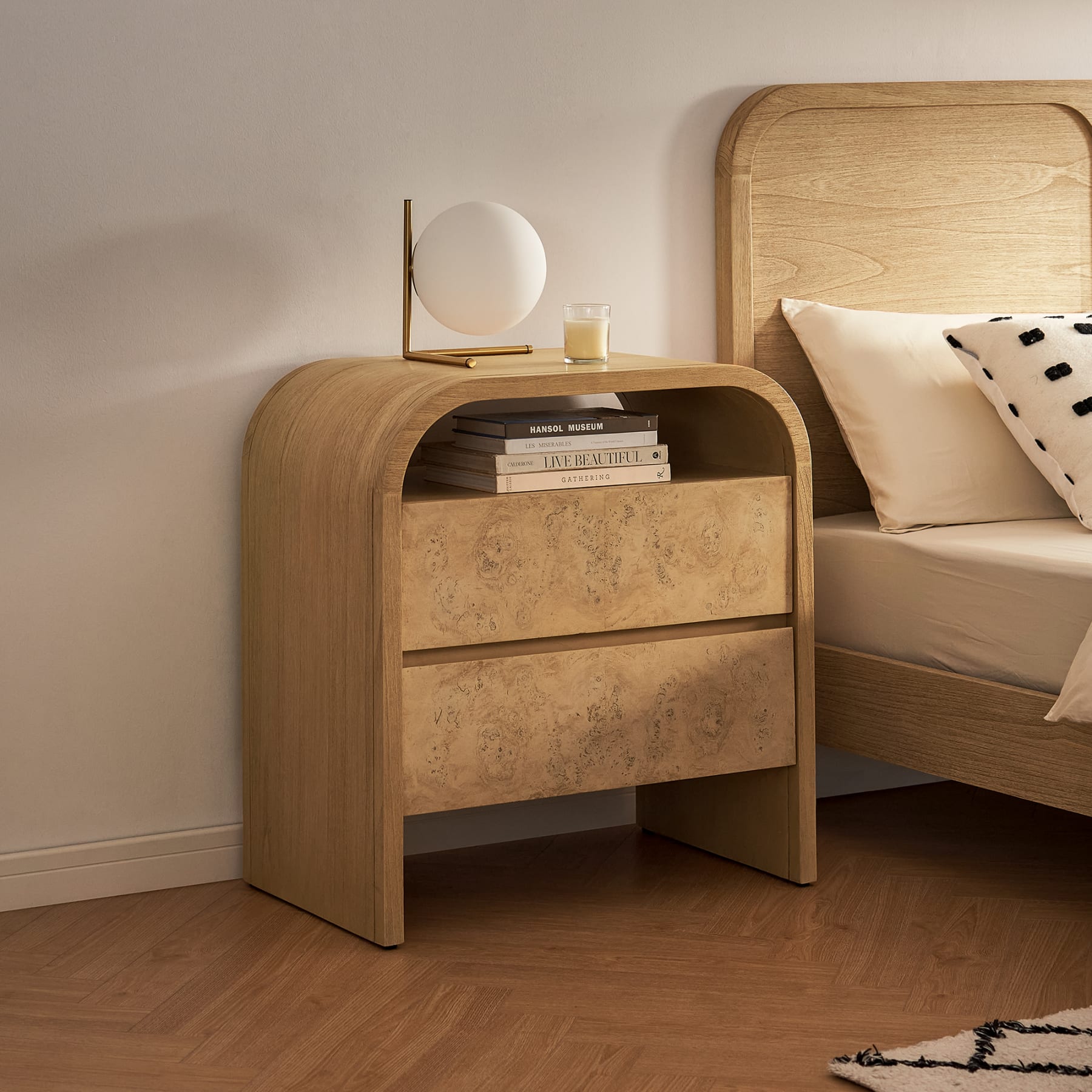 A 2-drawer nightstand with rounded edges next to a matching bed.