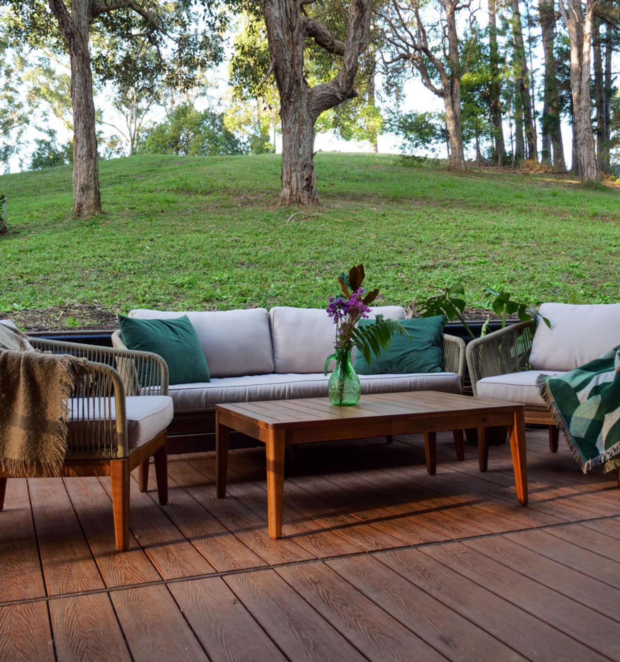 A matching woven outdoor sofa, lounge chairs, and a wooden coffee table placed in a backyard.