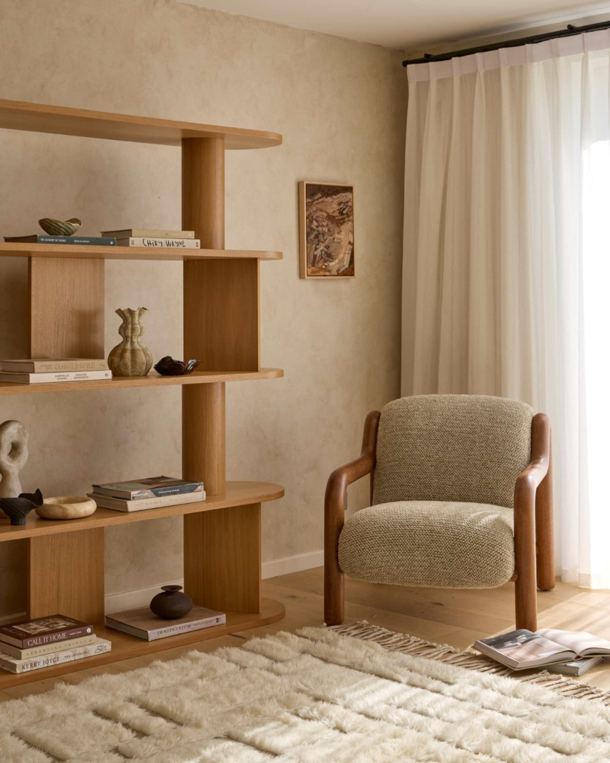 A wooden bookshelf with rounded shelves placed to an armchair with a plush rug underfoot.