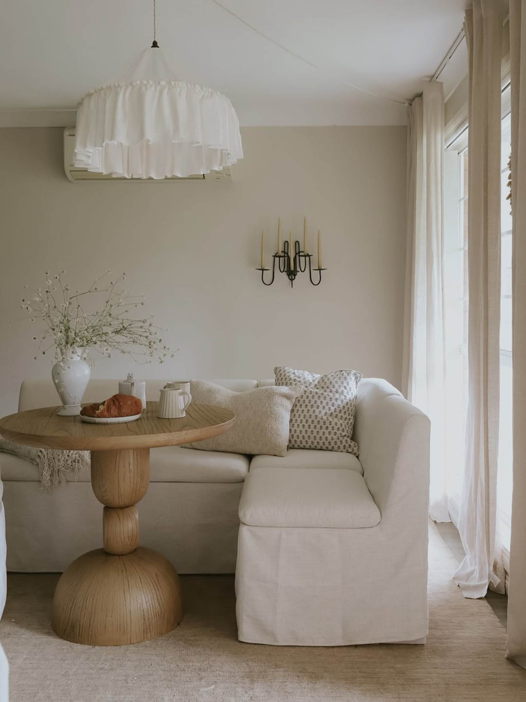 A round wooden dining table with a pedestal base placed in a dining area with an L-shape storage banquette.