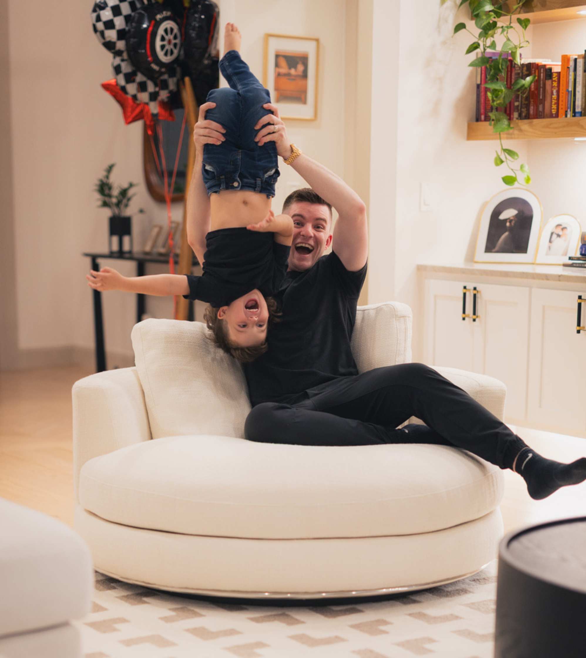 A man carrying a child upside down while seated on a large swivel armchair.