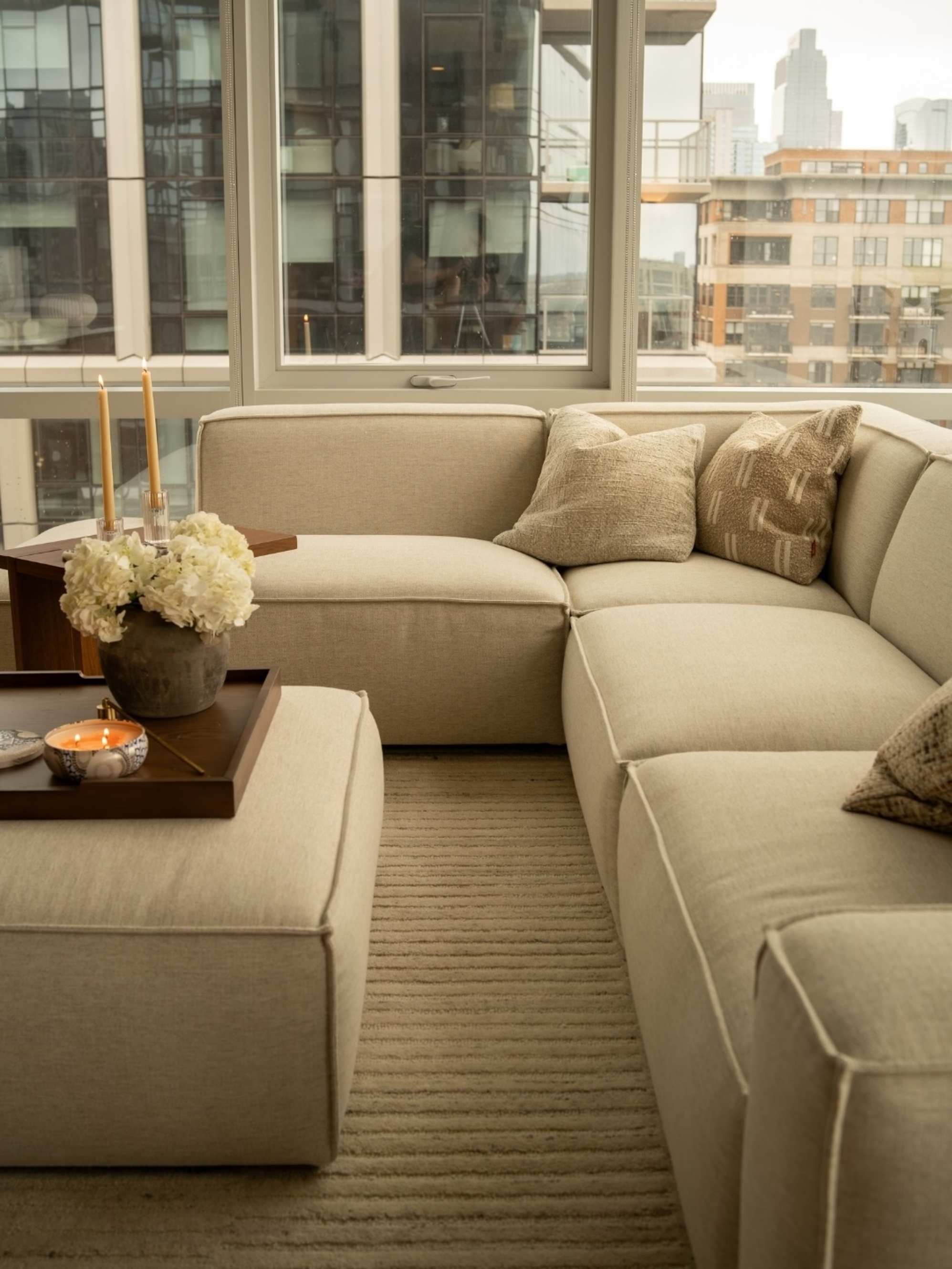 An L-shape sectional sofa with a matching ottoman placed infront of floor-length windows in a living room.