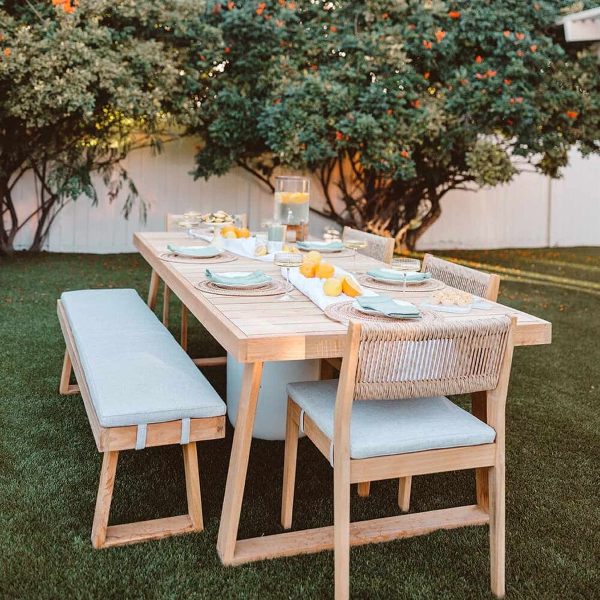 A teak dining table with a matching bench and dining chairs.