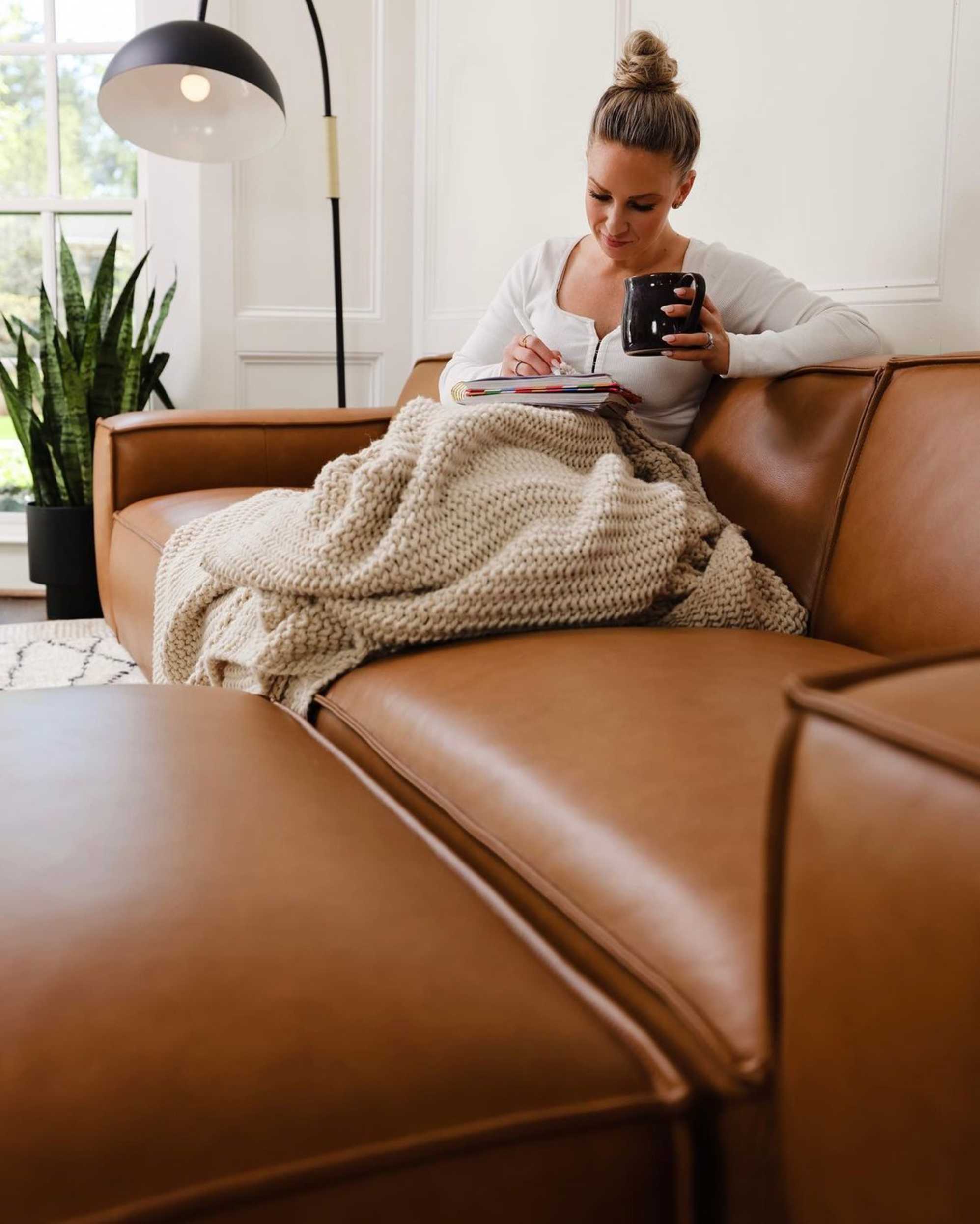 A person sitting on a leather sofa with a mug in hand.