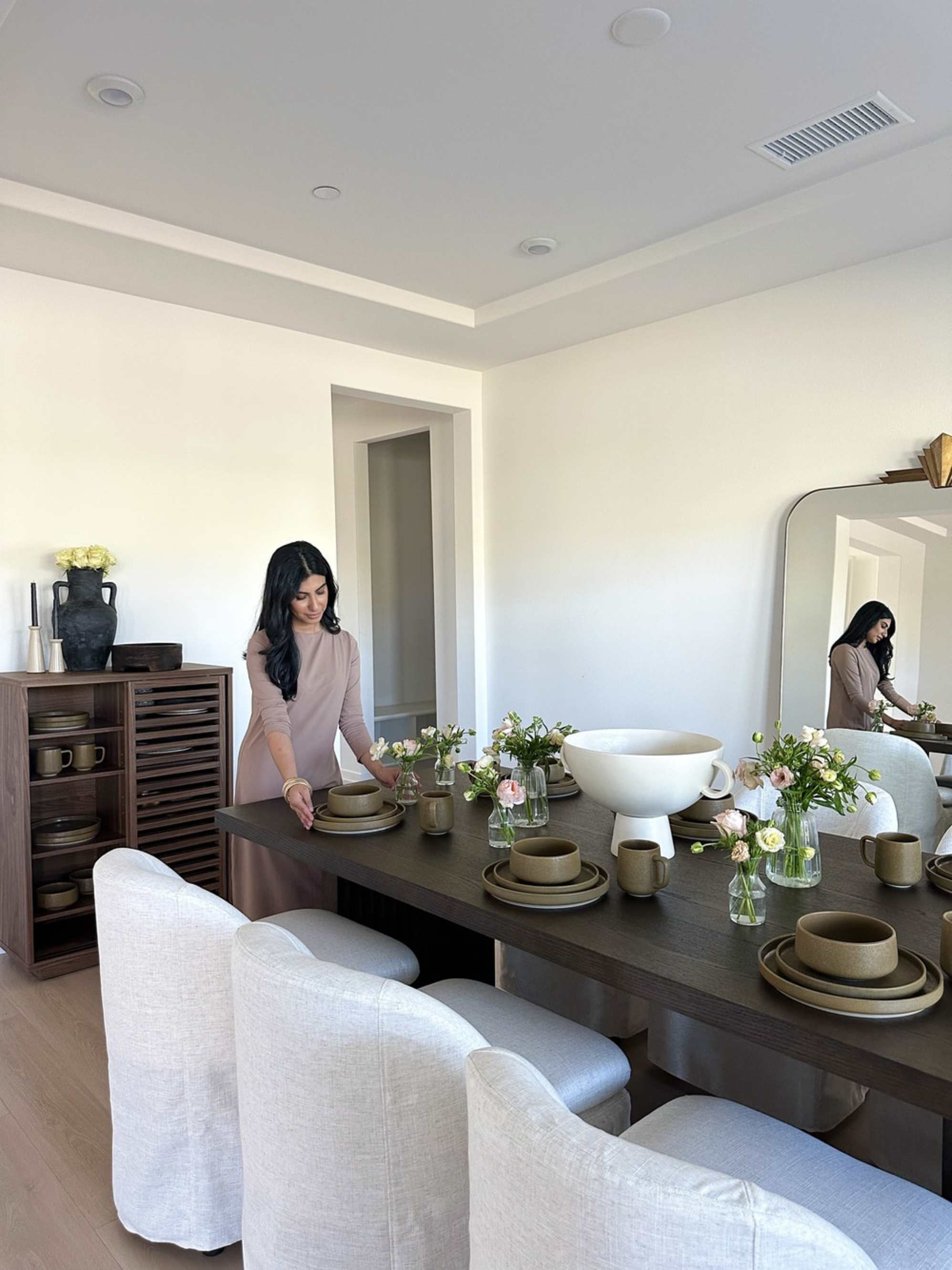 A person arranging dinnerware on a black rectangular dining table.