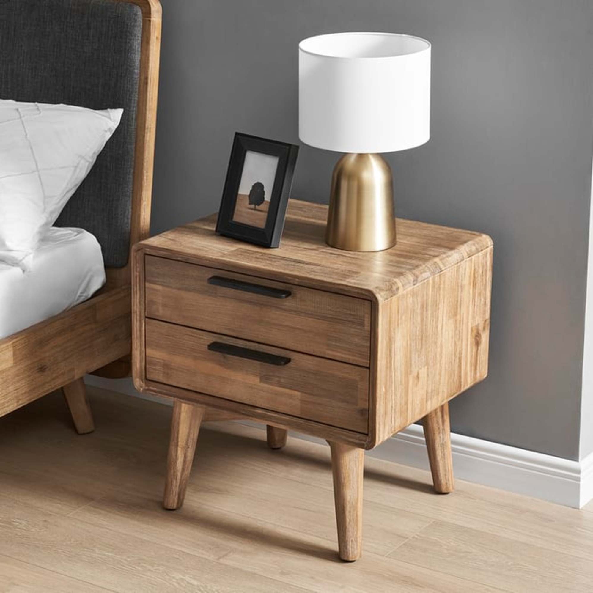 An acacia wood 2-drawer nightstand beside a matching bed.
