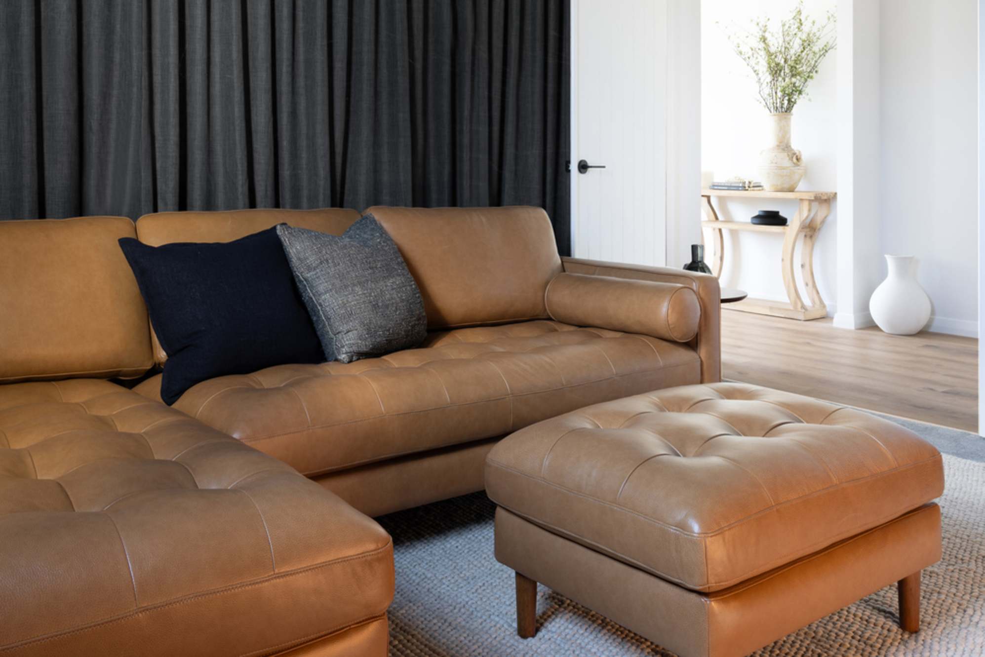 A leather chaise sectional sofa with a matching ottoman and two throw cushions.