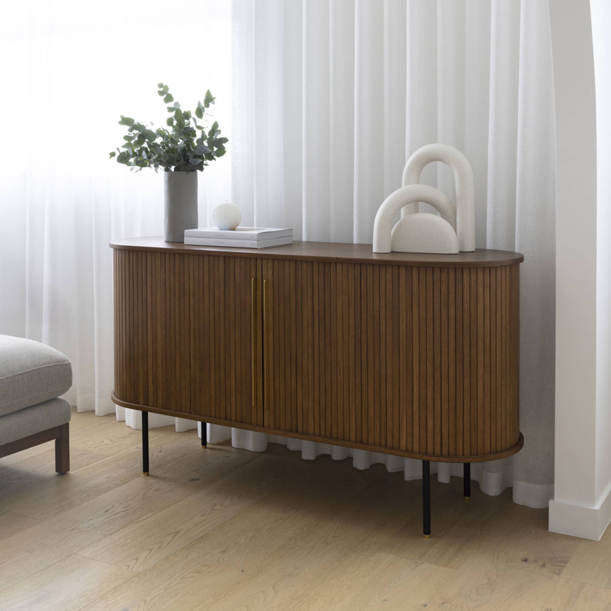 A sideboard placed in front of sheer curtains in a living room. 