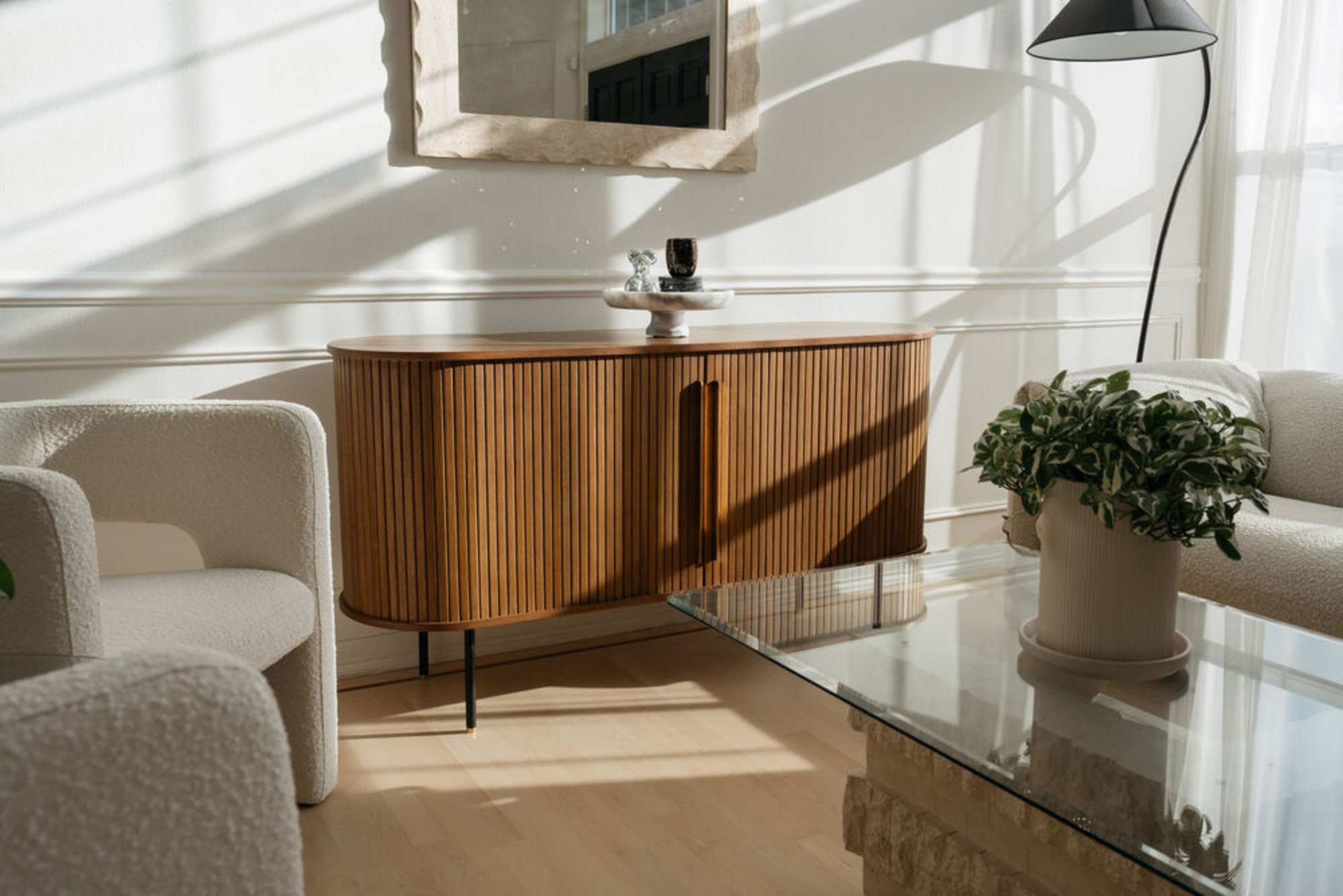 A sideboard placed in a living room with a mirror hung above it.