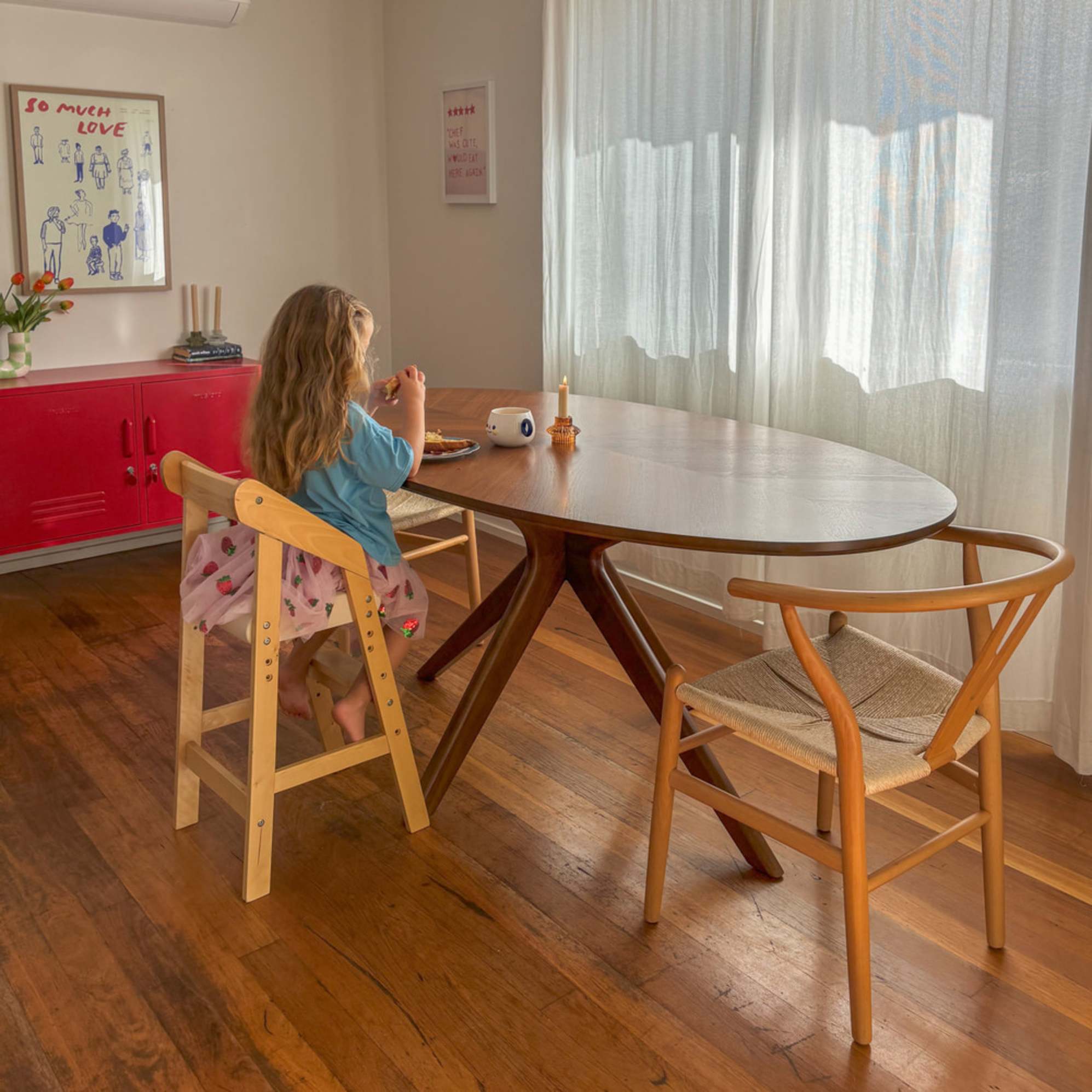 A child sitting on a high chair at a wooden oval dining table. 