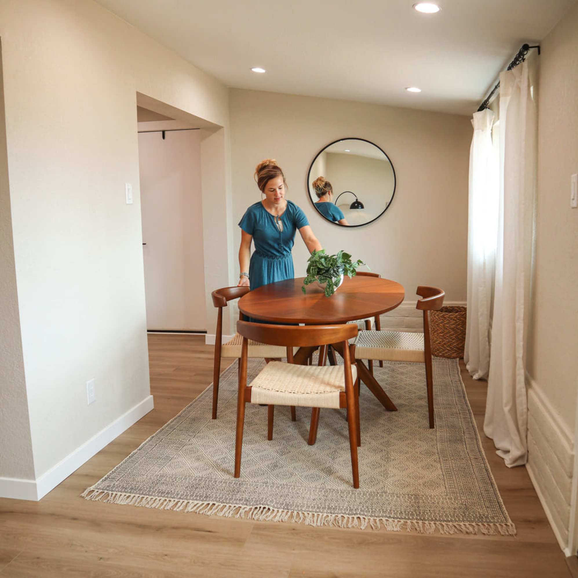 A person arranging a potted plant on an oval dining table.
