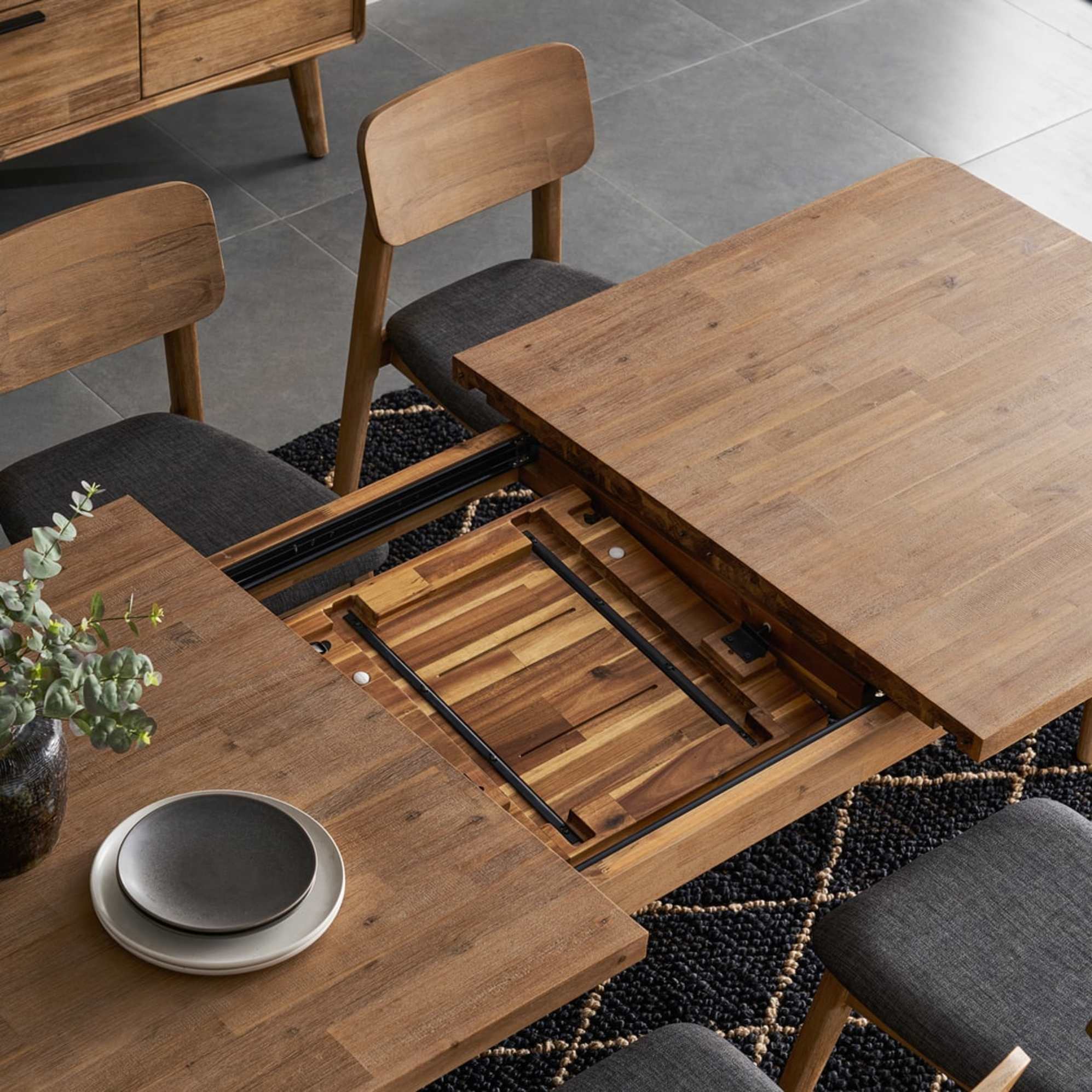 An acacia wood extendable dining table with a dropleaf mechanism.