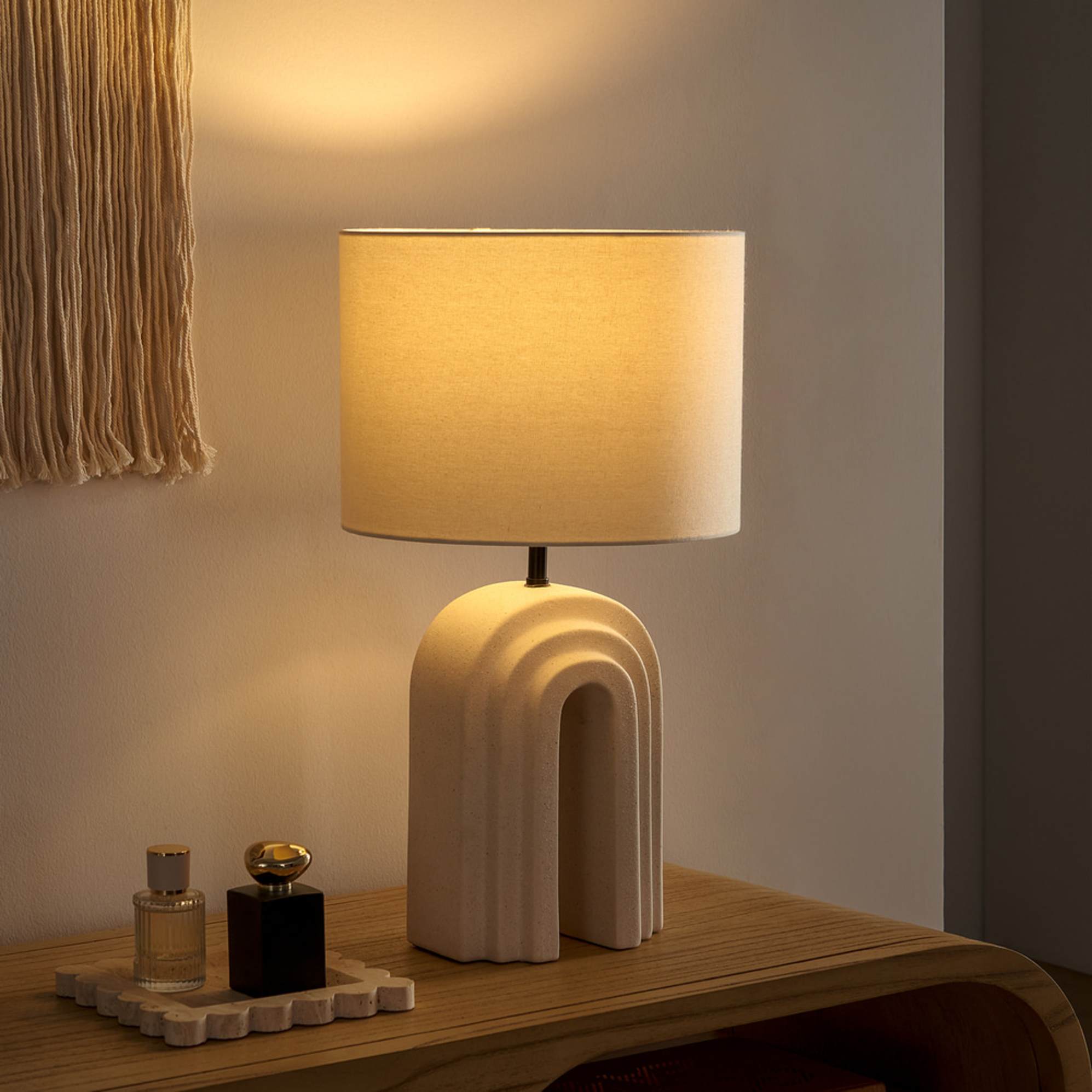 A table lamp with a sculptural arched base placed on a sideboard.
