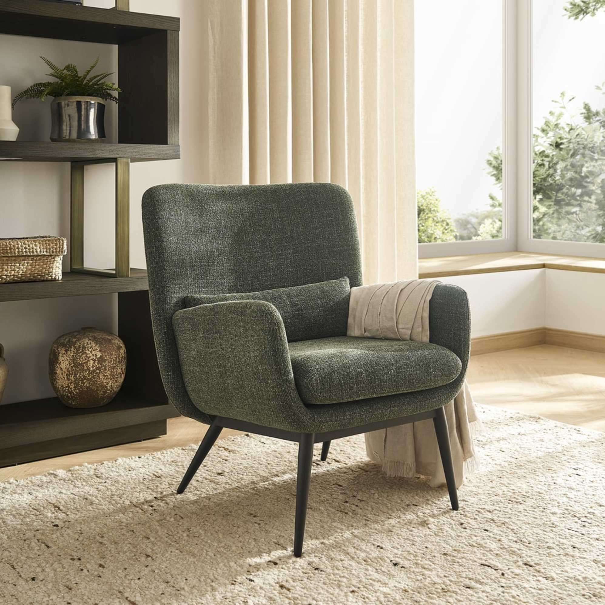A pine green armchair with a throw draped over one of its arms. 