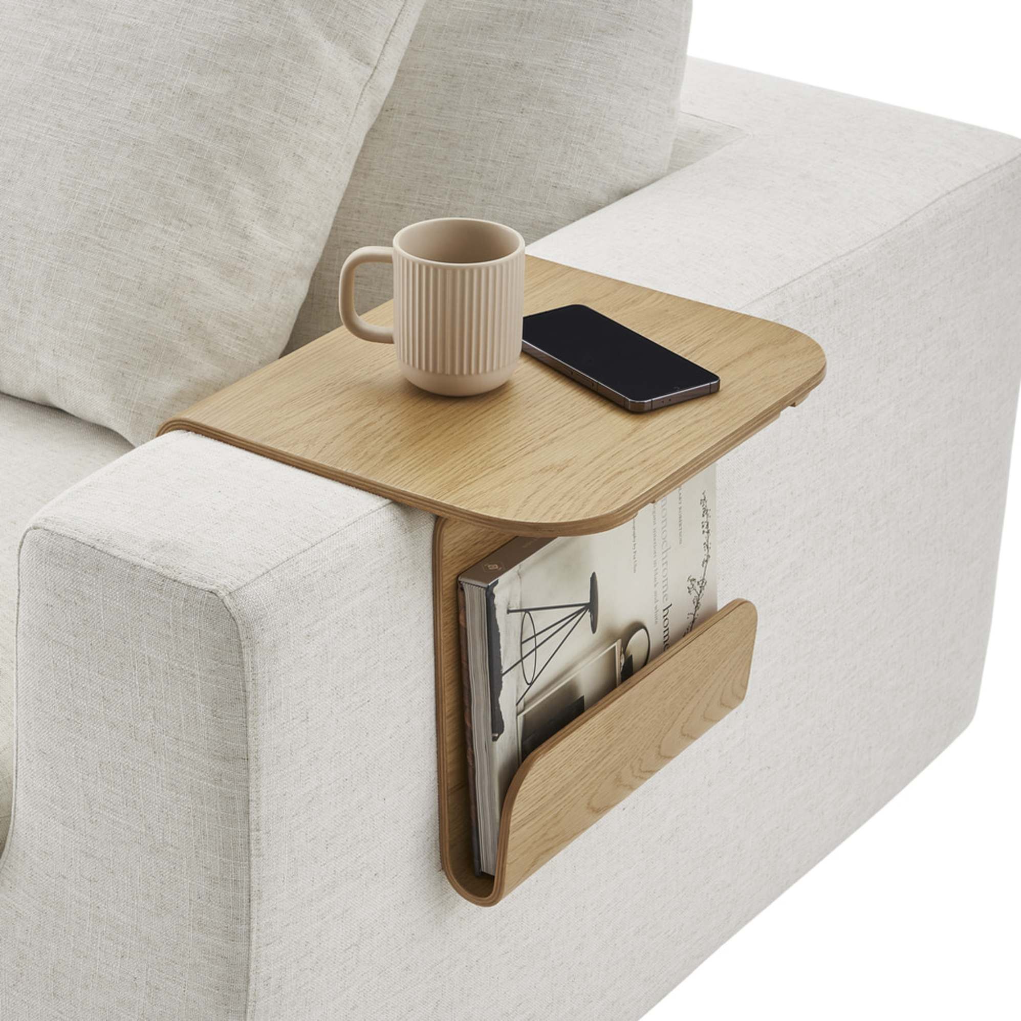 A wooden sofa armrest table with a mug, phone, and magazines.